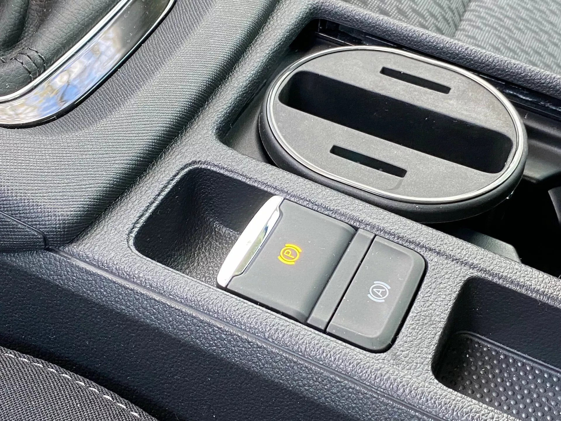 Gros plan de la console centrale de la Skoda Octavia 2020 avec un chargeur sans fil, un bouton de contrôle de la circulation d'air, un bouton de sécurité du véhicule, un compartiment de rangement partiellement ouvert avec revêtement en caoutchouc et un levier de vitesses avec accent chromé.