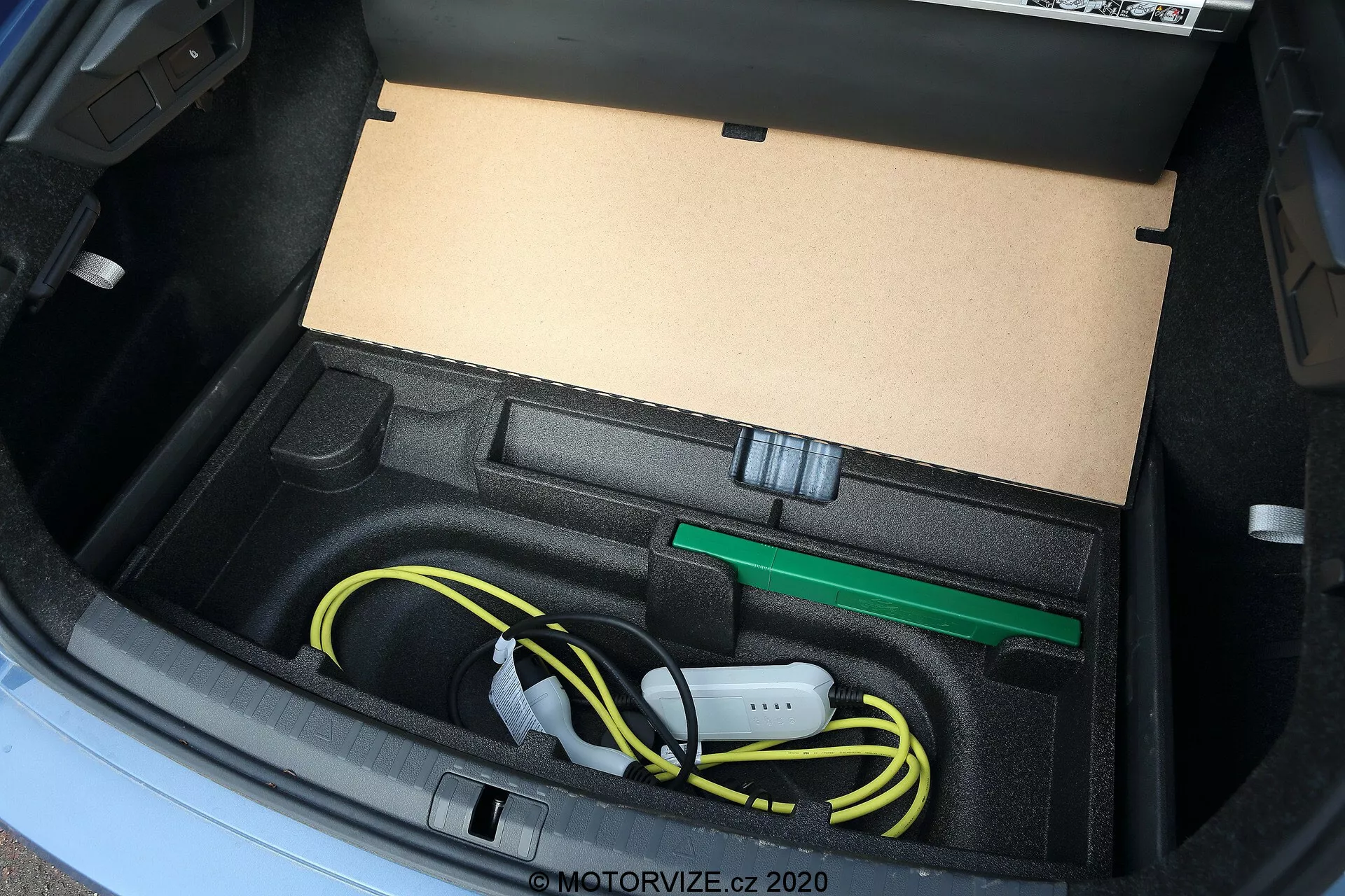 Vue rapprochée du coffre de la Skoda Octavia 2020, présentant un compartiment sur mesure conçu pour ranger le câble de charge du véhicule électrique et ses accessoires, y compris un câble de charge jaune enroulé et un crochet de remorquage vert, capturée d'un angle élevé avec un éclairage naturel.