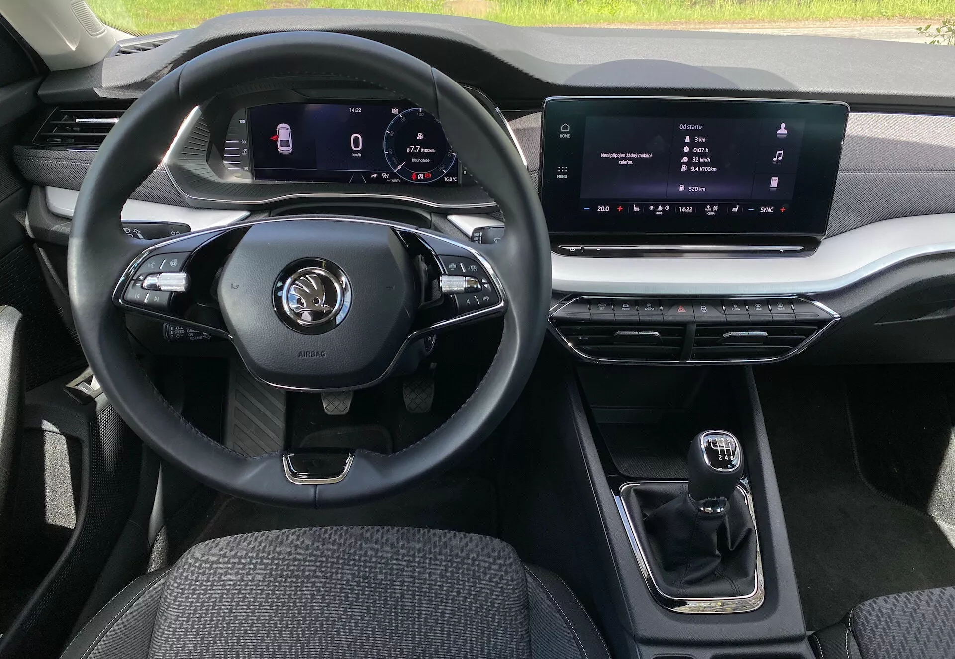Vue intérieure de la Škoda Octavia berline 2020 depuis la perspective du siège passager, mettant en évidence un volant multifonction à trois branches avec divers contrôles pour les médias et les appels mains libres, un tableau de bord numérique pour la navigation et les statistiques du véhicule, un écran tactile central d'infodivertissement, un levier de vitesses automatique compact, des accents métalliques sur les bouches d'aération et le système d'infodivertissement, une sellerie en tissu durable sur le siège du conducteur et un éclairage d'ambiance personnalisable.