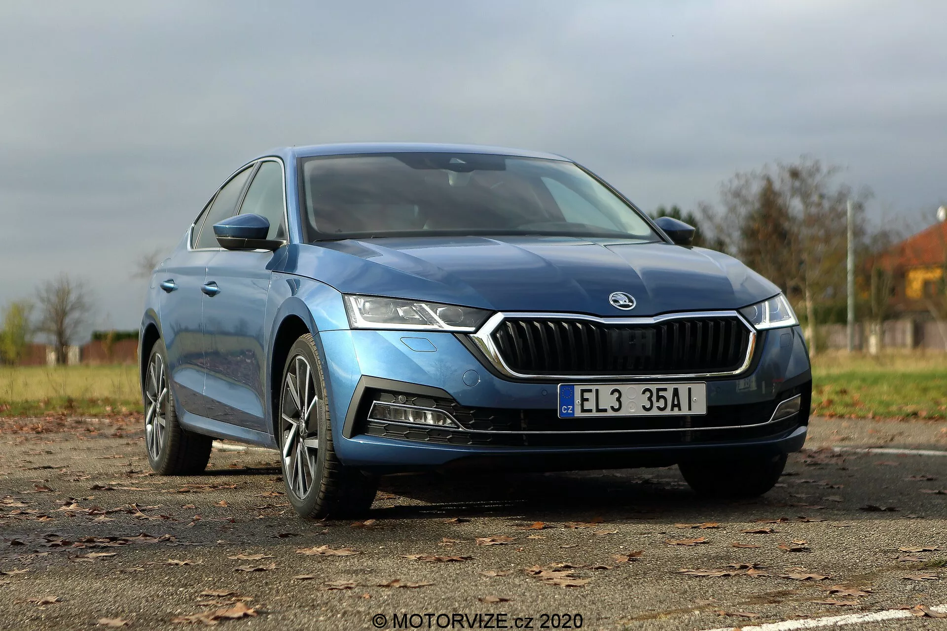 Image d'une Škoda Octavia Limousine bleue 2020 prise sous un angle avant trois-quarts bas, mettant en valeur la calandre avant contour chromé distinctif, les phares LED aigus, le capot profilé, les roues en alliage modernes et les rétroviseurs élégants avec indicateurs de direction intégrés. La carrosserie lisse et les vitres légèrement teintées sans cadre suggèrent un niveau de finition supérieur, tandis que toute la longueur de la voiture est affichée, y compris les badges visibles indiquant le modèle ou le type de moteur.