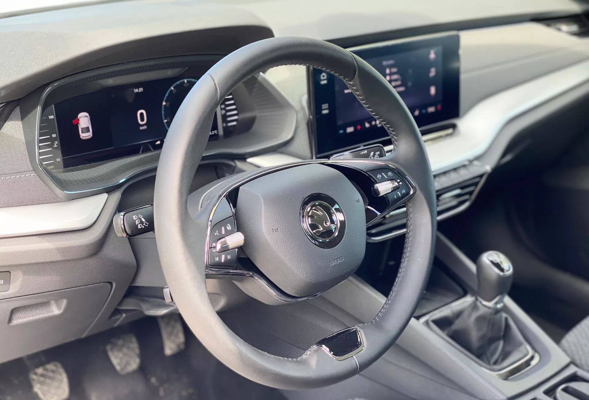 Image intérieure de la Škoda Octavia 2020 limousine centrée sur l'espace conducteur, montrant un volant à trois branches en cuir avec boutons de commande, tableau de bord numérique et système d'infodivertissement central depuis la perspective du passager avant.