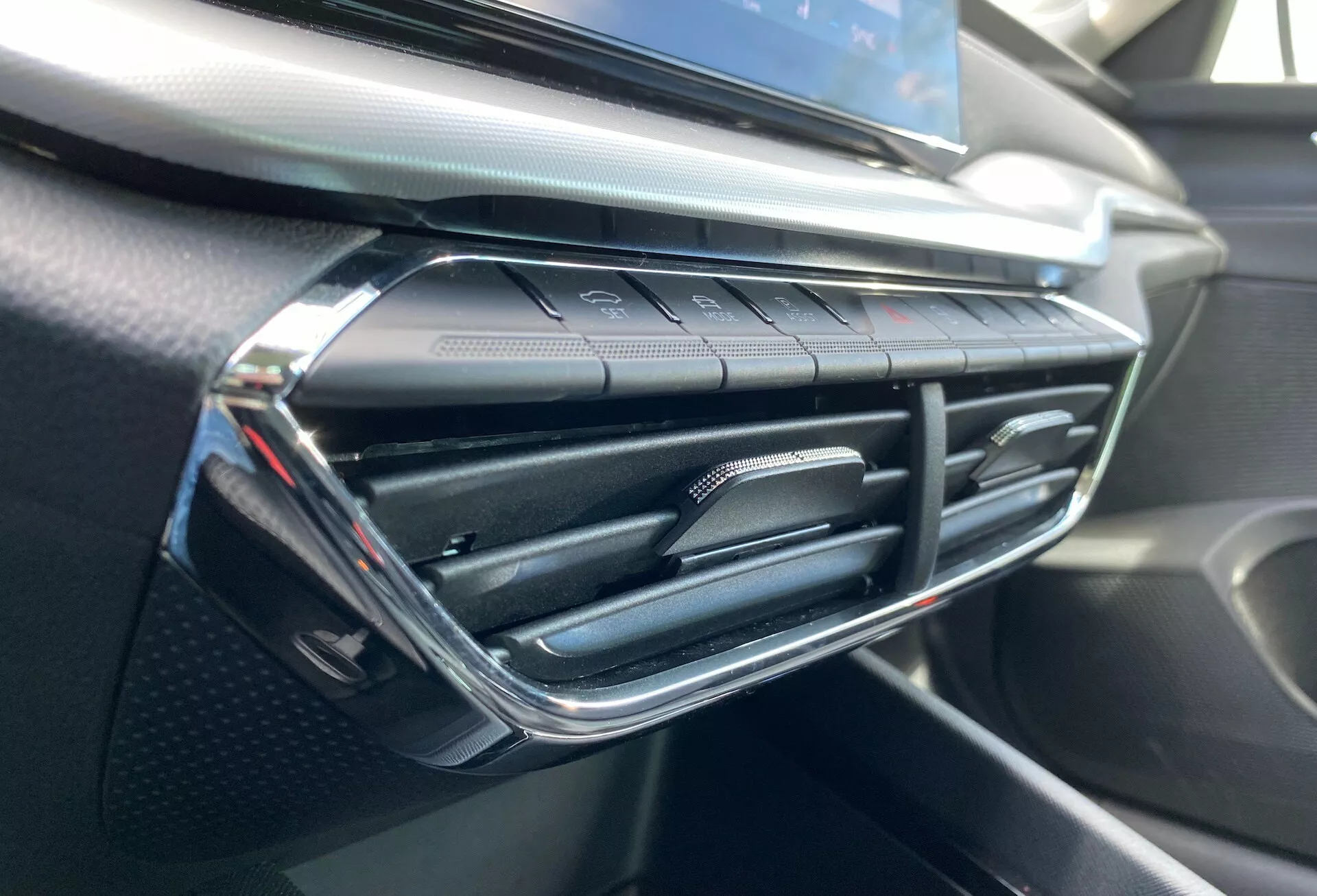 Vue rapprochée de l'intérieur de la Skoda Octavia 2020 mettant en avant la bouche d'aération de la climatisation et la zone environnante du tableau de bord, avec un design de bouche moderne orné d'accents chromés et de boutons de commande du climat tactile en dessous, sur un tableau de bord texturé à toucher doux et ressemblant à de la fibre de carbone.