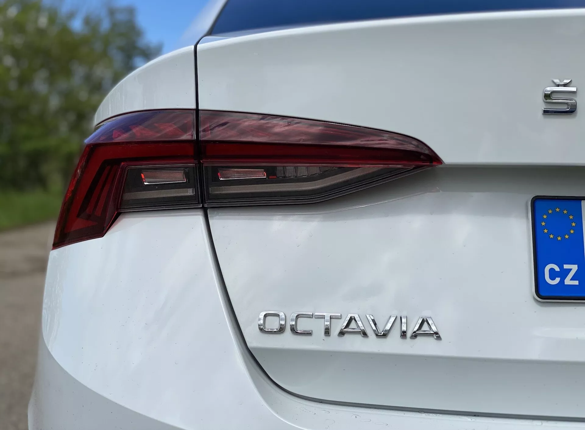 Vue latérale en gros plan sur le quart arrière d'une Škoda Octavia Limousine blanche 2020, mettant en avant le design angulaire des feux arrière à LED s'étendant sur le coffre, avec l'insigne 'Škoda' et le lettrage chromé 'OCTAVIA', avec une plaque d'immatriculation européenne (CZ) partiellement visible, capturée sous un angle bas.
