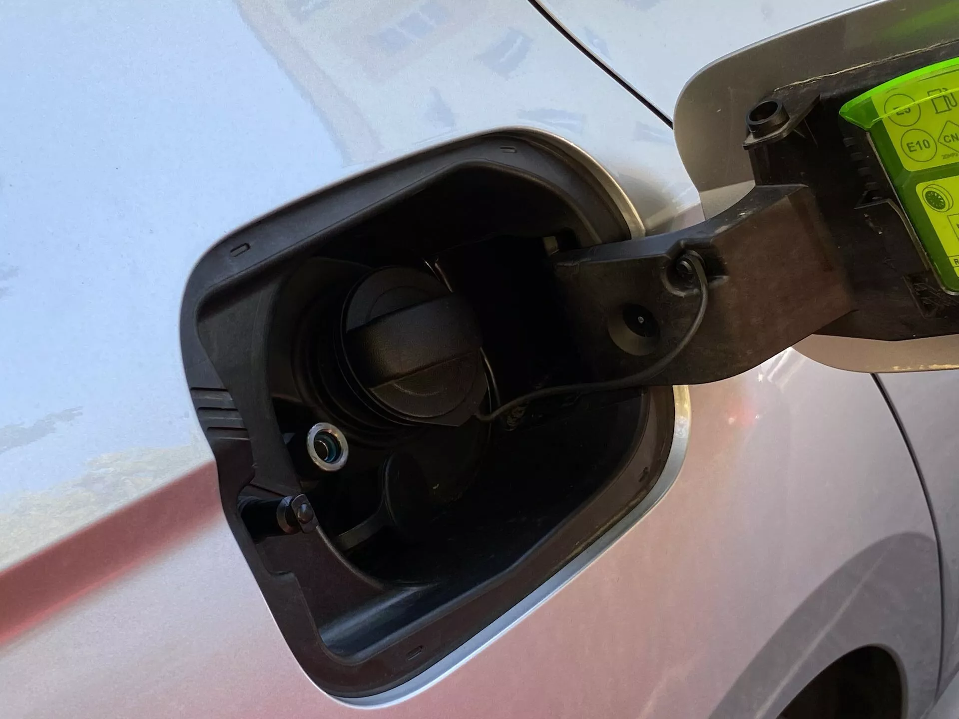 Gros plan sur la zone de remplissage de carburant d'une Skoda Octavia Limousine 2020, montrant le bouchon de carburant ouvert attaché par une sangle flexible, les détails environnants de la carrosserie du véhicule et le col de remplissage de carburant encastré avec une valve visible, le tout vu sous un léger angle vers le bas.