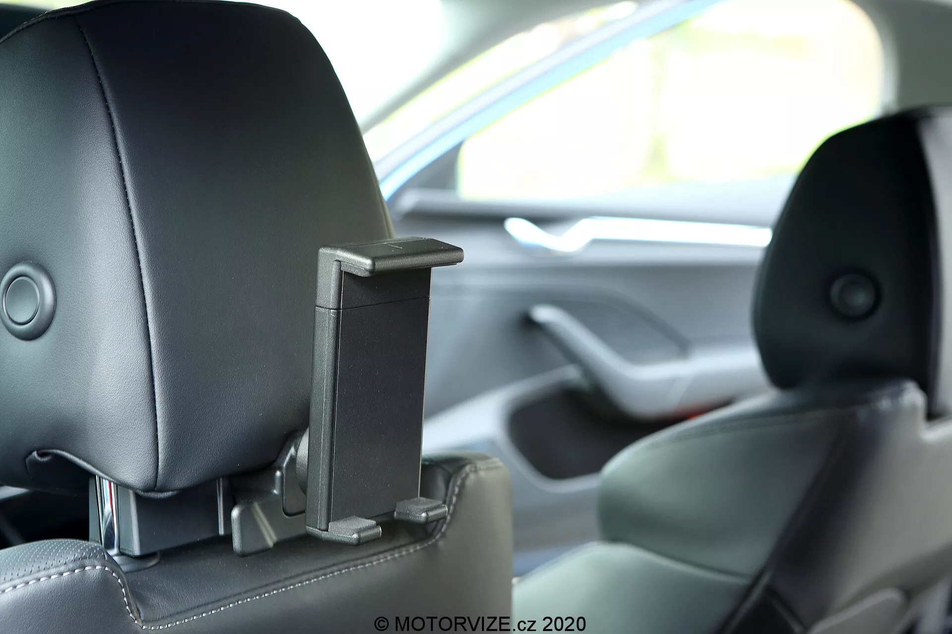 Vue intérieure d'une Skoda Octavia 2020 montrant l'appui-tête central arrière avec un composant rétractable intégré, peut-être une caractéristique de divertissement ou de sécurité. L'image capture l'appui-tête depuis la perspective d'un passager arrière au niveau des yeux avec une faible profondeur de champ, montrant la sellerie en cuir bicolore et mettant en avant le design technologique et ergonomique avancé.