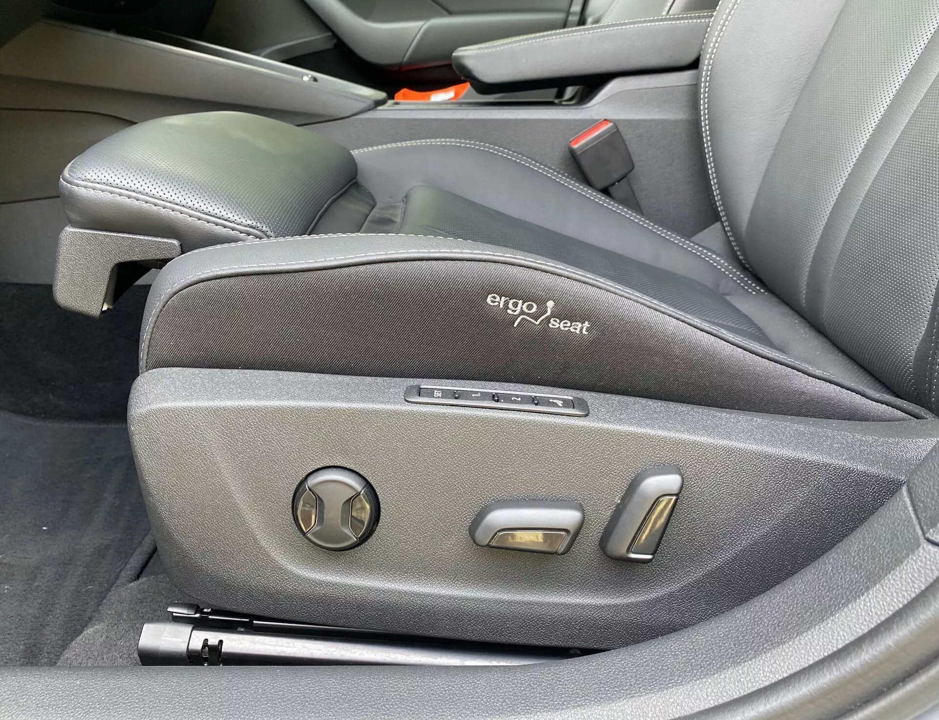 Vue en gros plan des commandes latérales du siège conducteur de la Skoda Octavia 2020, affichant un design ergonomique avec une sellerie en tissu foncé, un badge 'ergo seat' visible et des commandes de réglage électroniques comprenant un ajusteur d'inclinaison circulaire et deux boutons de positionnement métalliques, mettant en valeur l'intérieur premium et technologiquement avancé du véhicule.