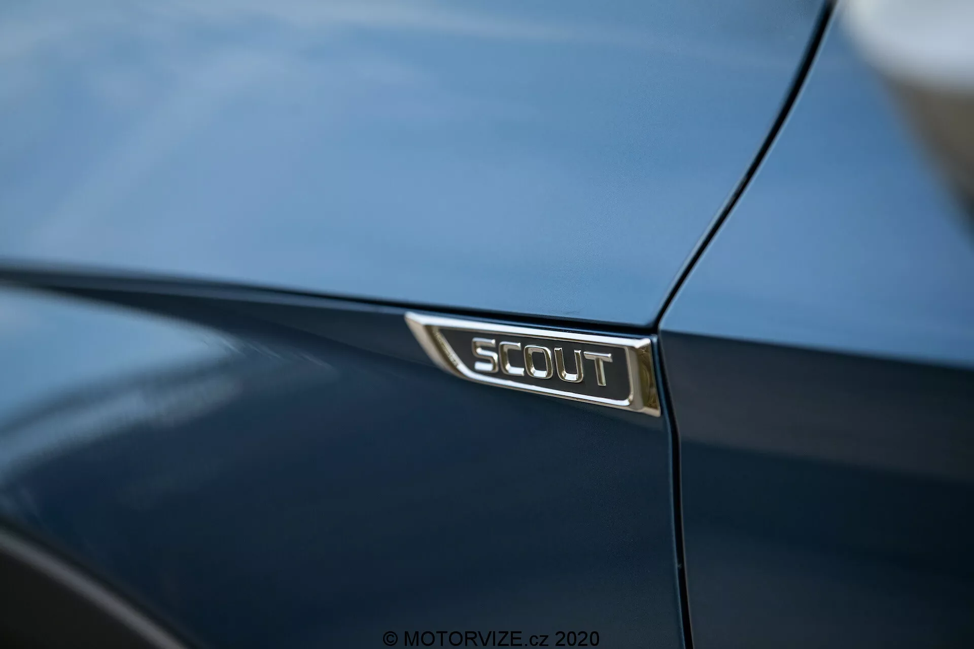 Gros plan sur le badge SCOUT sur une Škoda Octavia 2020 bleu foncé, montrant l'édition spéciale du véhicule avec des lettres argentées sur un fond noir, reflétant les détails luxueux et la finition brillante de la peinture.