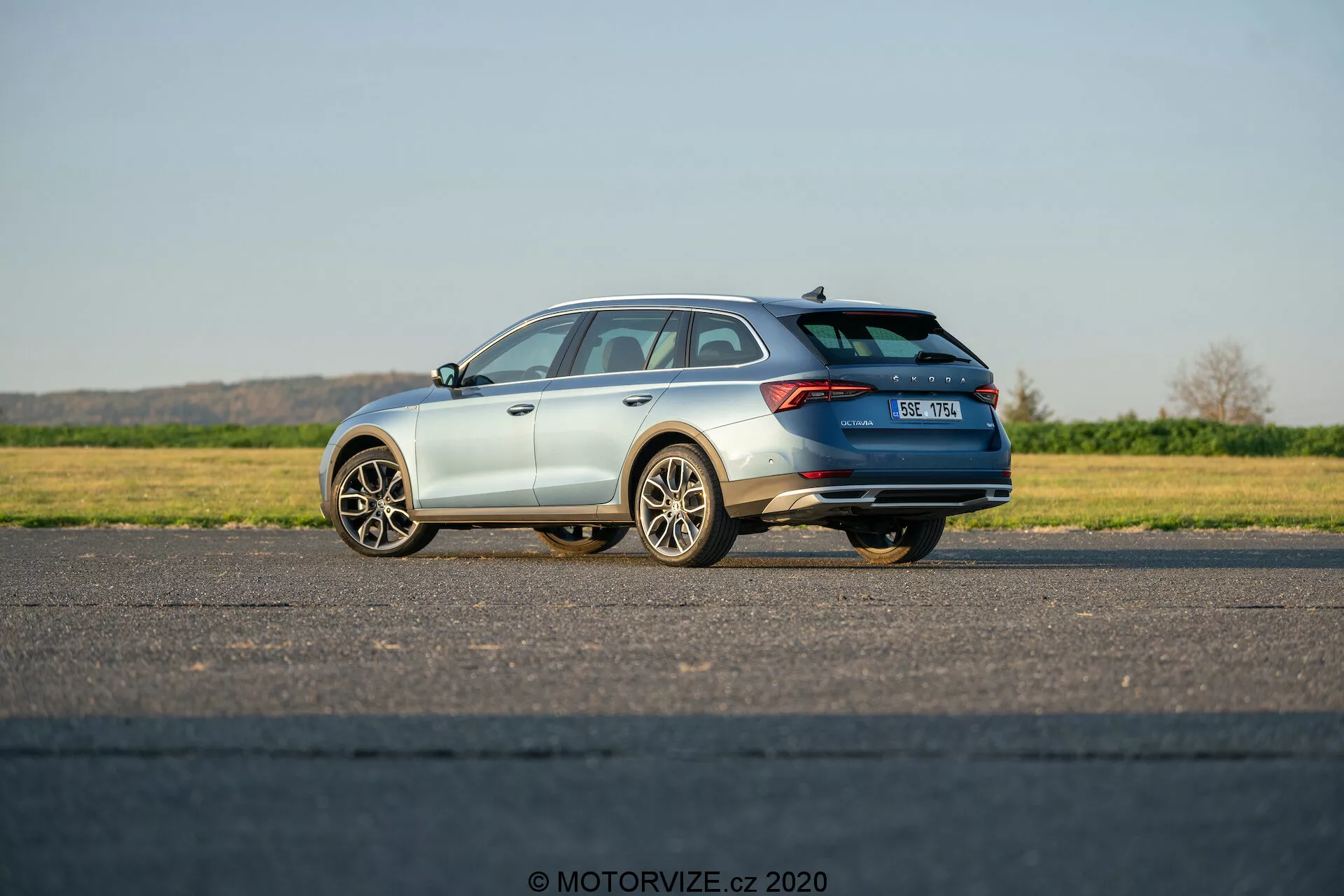 L'image montre une Škoda Octavia Scout 2020, un break moderne, capturée en vue arrière trois quarts. Elle met en évidence les éléments de conception de la voiture, y compris les feux arrière horizontaux s'étendant vers le centre du hayon, le spoiler de toit, les rails de toit et les roues en alliage à plusieurs branches. Positionnée sur une surface pavée plane, avec le côté conducteur plus proche de l'appareil photo, la voiture affiche sa finition de peinture métallique et une partie de son système d'échappement. La plaque d'immatriculation est légèrement floue et le badge Škoda est visible. La photo prise à la lumière naturelle du jour sous un ciel clair montre un véhicule à l'arrêt avec d'éventuelles fonctionnalités technologiques cachées telles que l'assistance au stationnement, les caméras de recul ou les systèmes d'évitement des collisions.