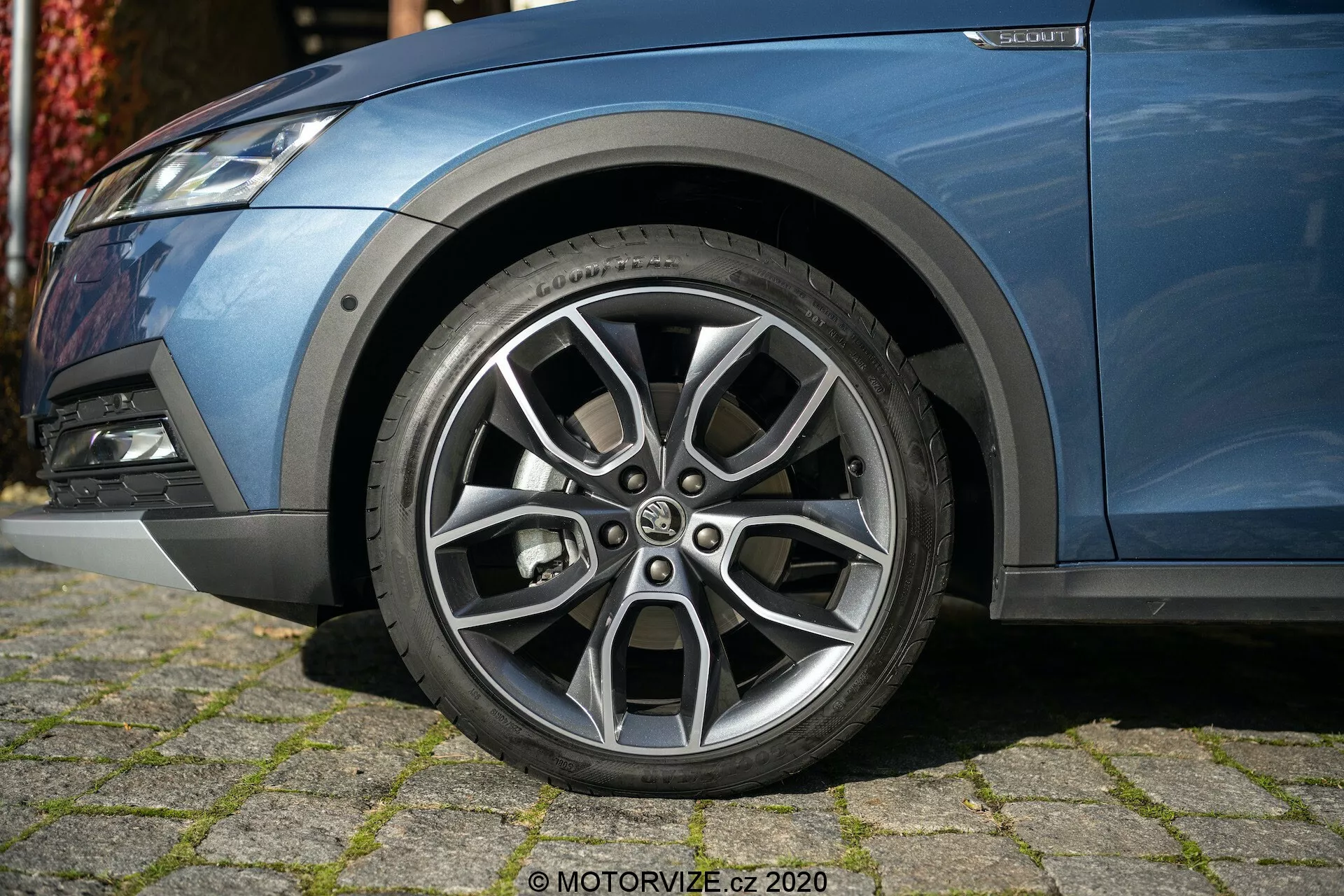 Vue rapprochée du côté avant gauche d'une Skoda Octavia 2020 (Octavia-Scout) mettant l'accent sur sa roue en alliage méticuleusement conçue avec un design à plusieurs rayons, une finition argentée contrastante et des motifs de bande de roulement visibles. La photo, prise sous un angle bas, capture une partie de la carrosserie métallique bleue de la voiture, le pare-chocs avant avec feu antibrouillard et les composants de la suspension, montrant son apparence moderne et sportive.