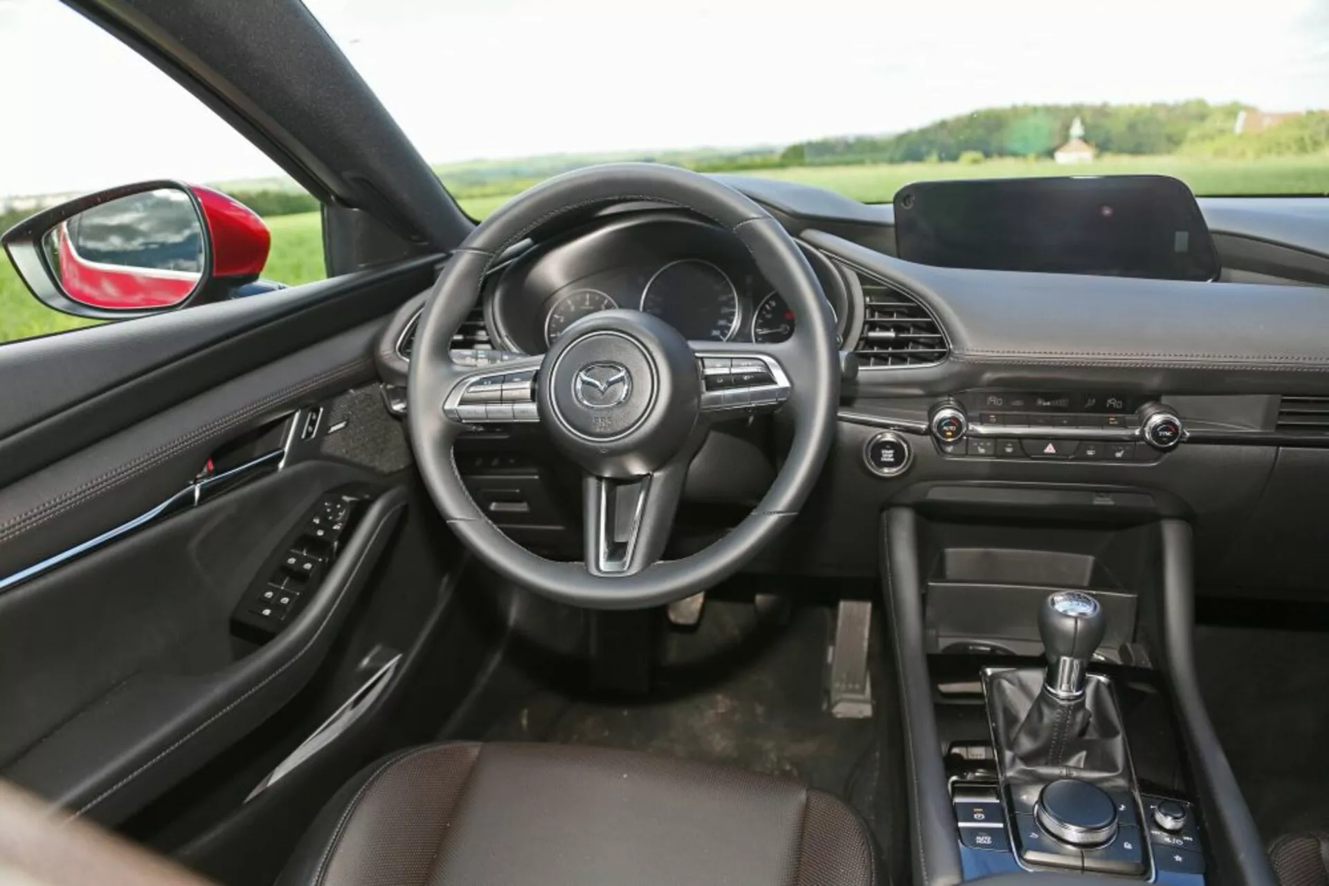 Vue intérieure d'une Skoda Scala 2019 depuis le siège arrière mettant en lumière le tableau de bord, le volant, la console centrale, le levier de vitesse manuel et la conception de la cabine avant avec des fonctionnalités technologiques et de confort.