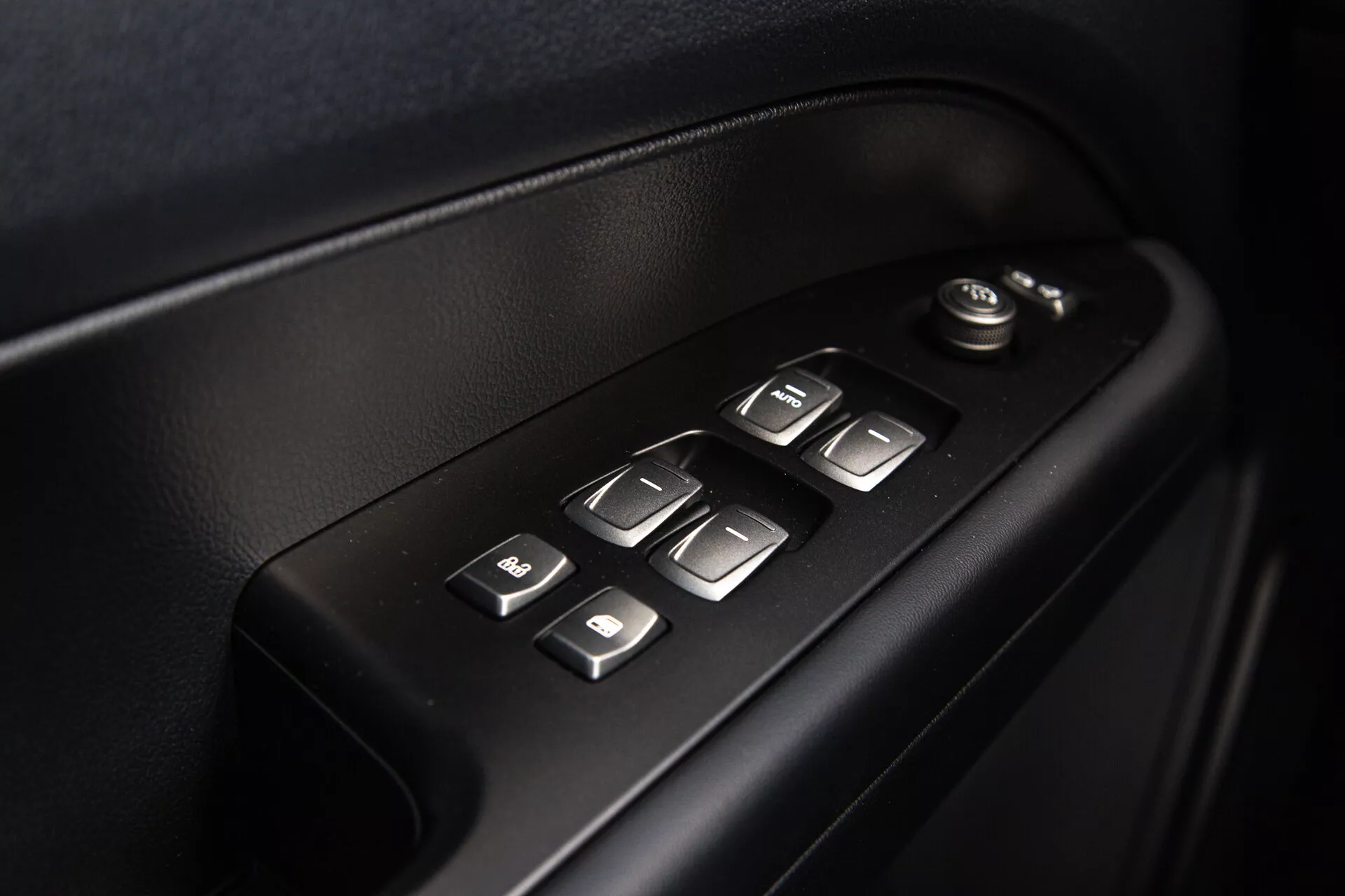 Vue rapprochée des commandes de porte intérieure du SsangYong Musso 2022 montrant les réglages électriques des fenêtres et des miroirs, boutons éclairés pour faciliter l'utilisation, dans un design ergonomique de haute qualité