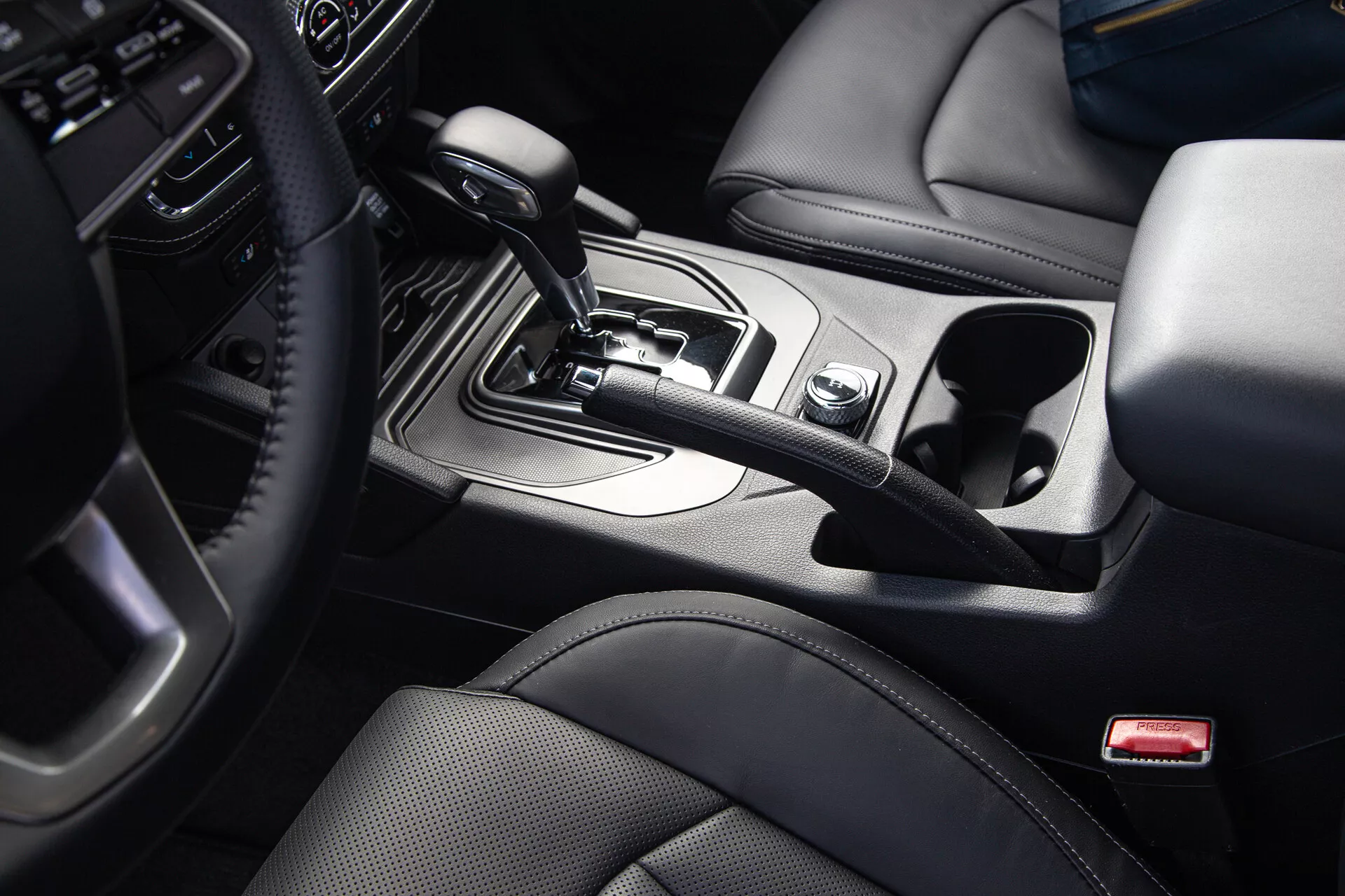 Pick-up SsangYong Musso Grand 2022 offrant une vue en plongée légèrement angulée de la console centrale avec un sélecteur de vitesse automatique en position 'Park', entouré par les commandes d'infodivertissement et de modes de conduite, avec accoudoir revêtu de cuir et accents à finition métallique design.