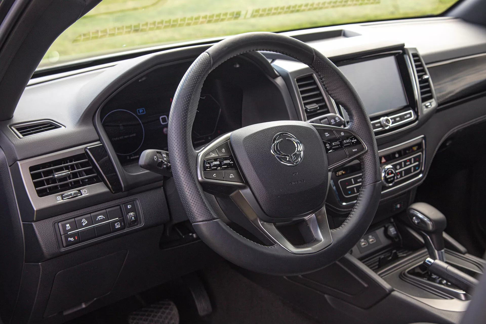 Photo intérieure du SsangYong Musso 2022 montrant le côté conducteur, comprenant le volant multifonction à trois branches, le tableau de bord numérique et le système d'infodivertissement central sur le tableau de bord depuis la perspective du passager arrière
