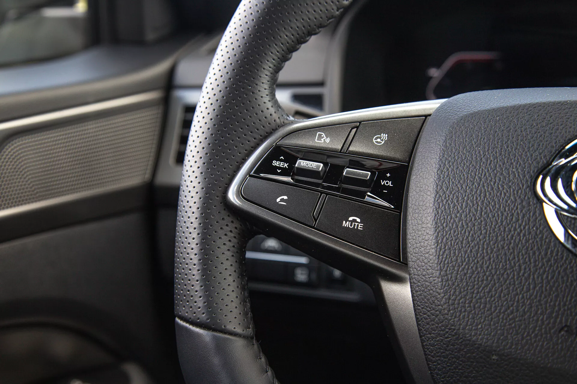 Vue rapprochée des commandes situées sur le côté gauche du volant du SsangYong Musso 2022 avec poignée en cuir perforé et boutons technologiques montés pour le confort et la sécurité du conducteur
