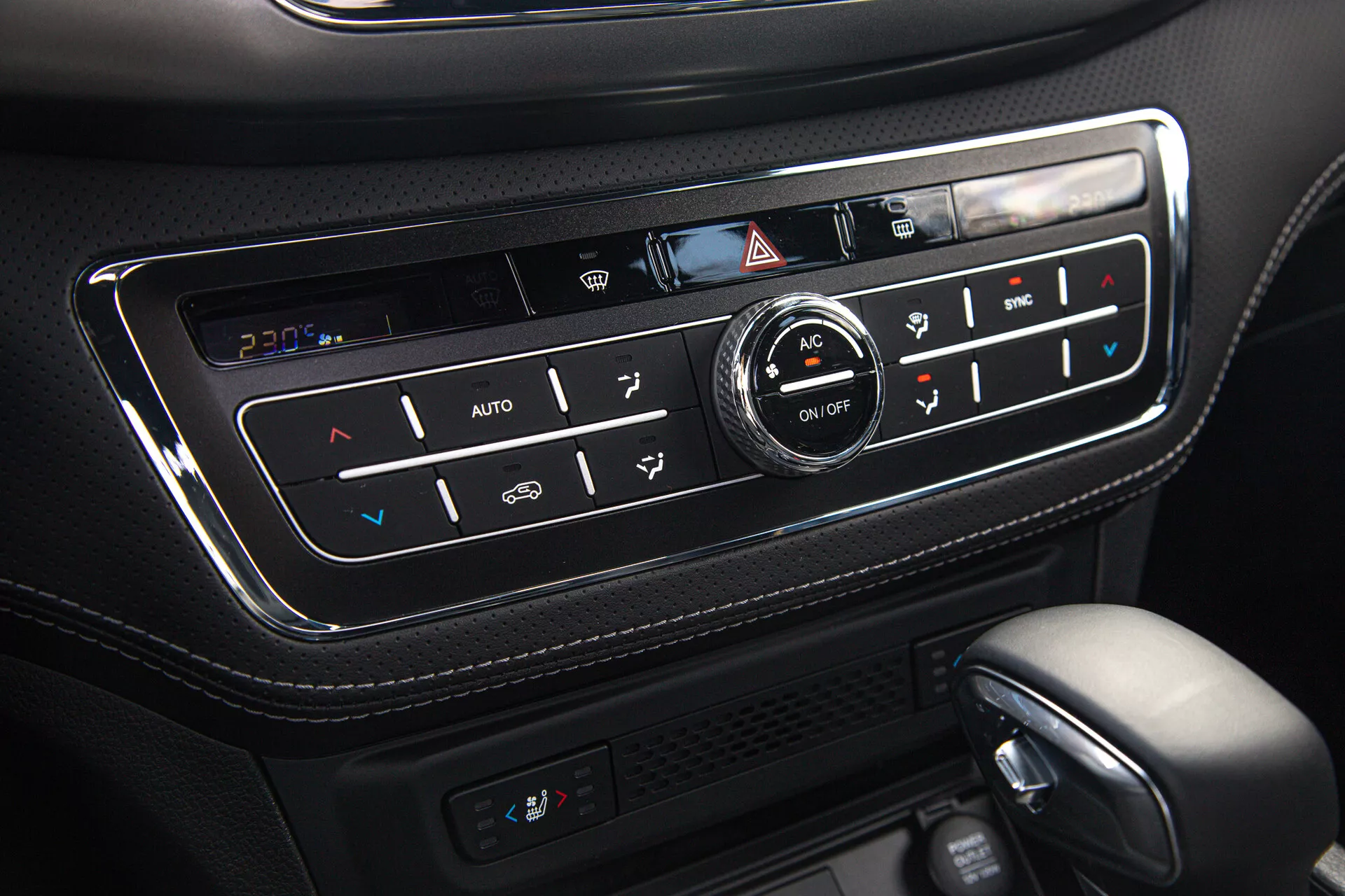 Vue rapprochée du panneau de contrôle climatique du SsangYong Musso 2022 Grand Pick-up montrant le système de réglage automatique de la température, le contrôle bi-zone, fonctionnalité de sièges chauffants, réglages AC et de dégivrage, inséré dans une console en cuir noir de haute qualité avec finition brillante et boutons rétroéclairés