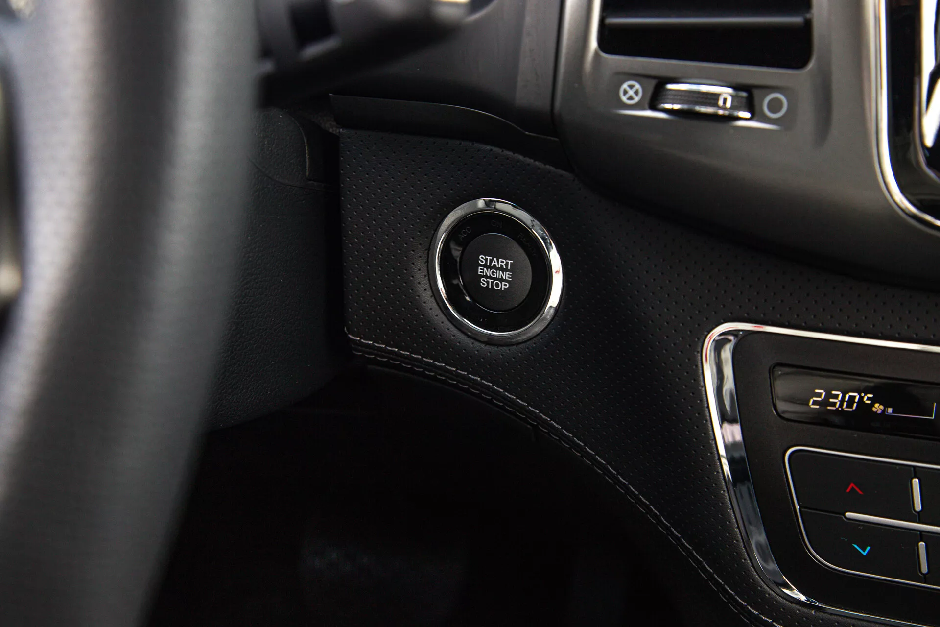 Vue rapprochée du bouton de démarrage/arrêt du moteur dans un SsangYong Musso 2022, mettant en avant le système d'allumage sans clé sur le tableau de bord avec fond de surface noire et détails de contrôle du climat