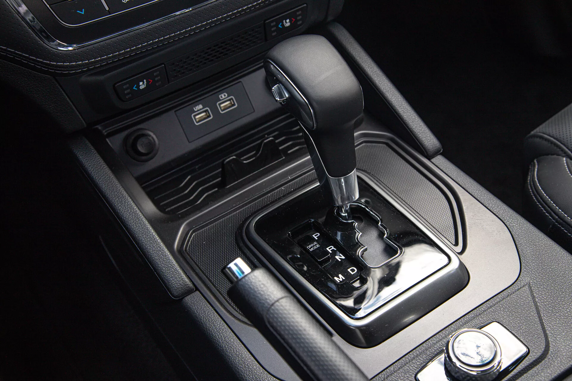 Intérieur du SsangYong Musso Grand Pickup 2022 montrant la console centrale avec sélecteur de vitesse automatique, ports de connectivité moderne et commandes des modes de conduite, encadré par des accents de cuir et de métal