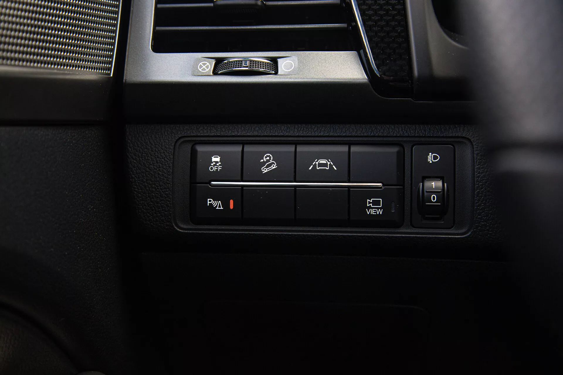 Gros plan sur les commandes intérieures du SsangYong Musso 2022, comportant des boutons rétroéclairés pour le contrôle de stabilité, capacités tout-terrain, assistance au stationnement ou à la voie, position du siège ajustable et informations sur le système