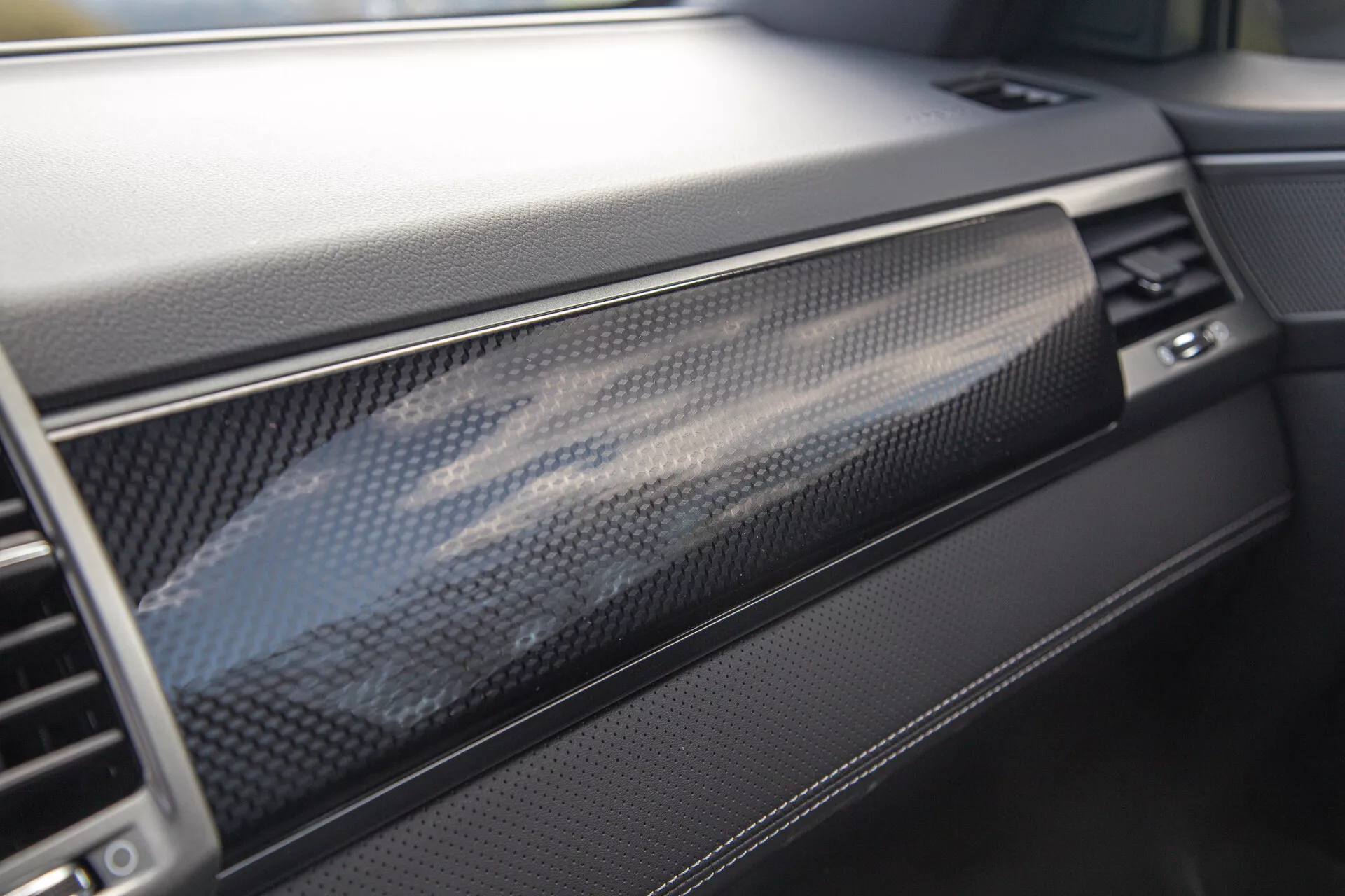 Vue rapprochée du tableau de bord du SsangYong Musso 2022 affichant un garnissage luxueux en fibre de carbone et des matériaux de haute qualité, axée sur le côté passager avec des aperçus du compartiment à gants, de la ventilation et du contrôle de température, illustrant l'accent mis par le véhicule sur le design intérieur moderne et la qualité de fabrication.