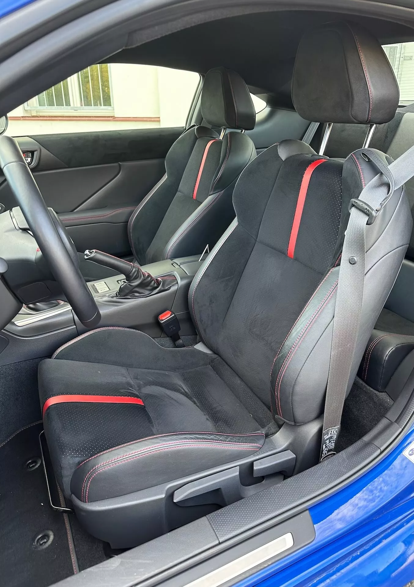 Vue intérieure de la Subaru BRZ 2023 mettant en lumière les sièges avant sportifs au design ergonomique et aux détails rouges, le sélecteur de transmission automatique et l'esthétique moderne du cockpit depuis une perspective extérieure oblique