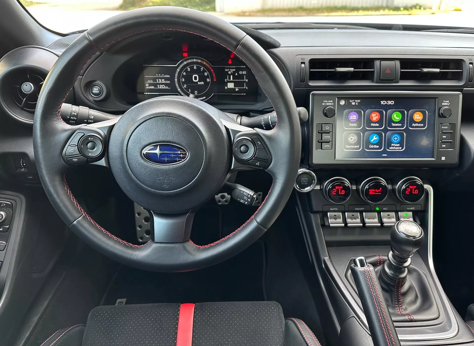 Intérieur du Subaru BRZ 2023 du point de vue du conducteur avec un volant sportif en cuir avec commandes multifonctions et coutures rouges, un tableau de bord avec cadrans analogiques et un écran numérique, une console centrale avec un grand écran tactile pour le système d'infodivertissement et contrôle climatique bi-zone, et un levier de vitesse manuel avec soufflet en cuir et accents rouges, sur un intérieur noir avec des accents rouges sportifs, mettant en évidence les fonctionnalités avancées du véhicule et la technologie.
