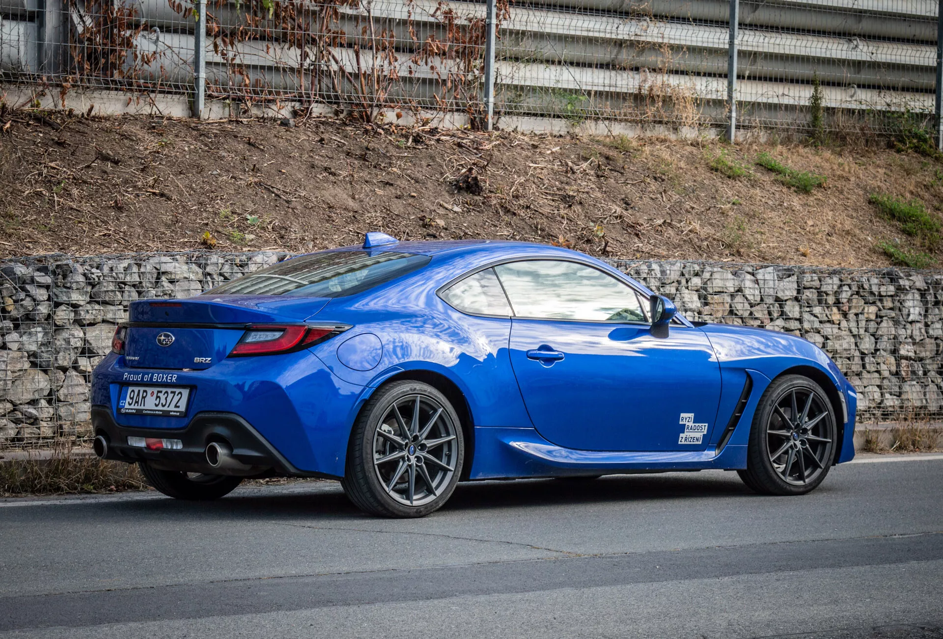 Coupé sportif Subaru BRZ 2023 de couleur bleu vif avec un design aérodynamique garé dans une rue, mettant en avant l'arche de roue arrière, les feux arrière, la courbure de la fenêtre arrière menant au couvercle du coffre, les lignes sculptées, la ligne de toit inclinée, les roues en alliage à plusieurs branches, les freins performants, l'aileron arrière profil bas, les doubles pots d'échappement dans le diffuseur arrière, les rétroviseurs de couleur carrosserie et un capot long et sportif.