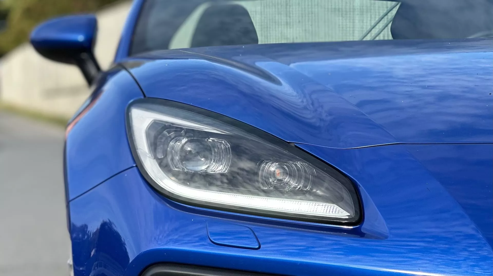 Vue rapprochée du phare côté conducteur de la Subaru BRZ 2023, présentant un éclairage LED ou HID, des lentilles projecteurs, et une prise d'air sportive contre une carrosserie bleu métallique