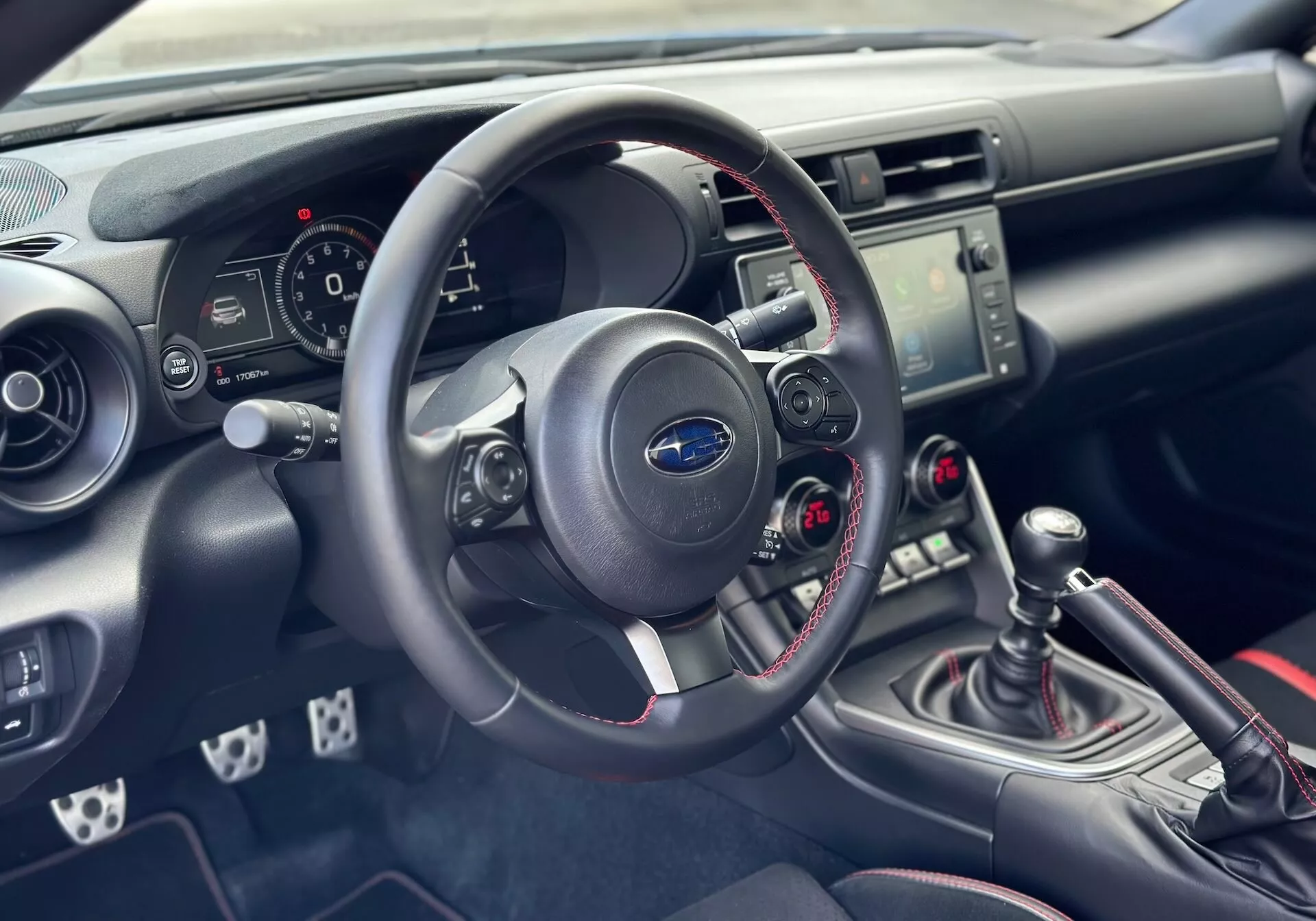 Intérieur de la Subaru BRZ 2023 se concentrant sur le tableau de bord et le cockpit côté conducteur avec vue détaillée du volant, du bloc instruments, de la console centrale avec commandes audio et climatisation, et du levier de vitesse manuel avec coutures rouges sportives
