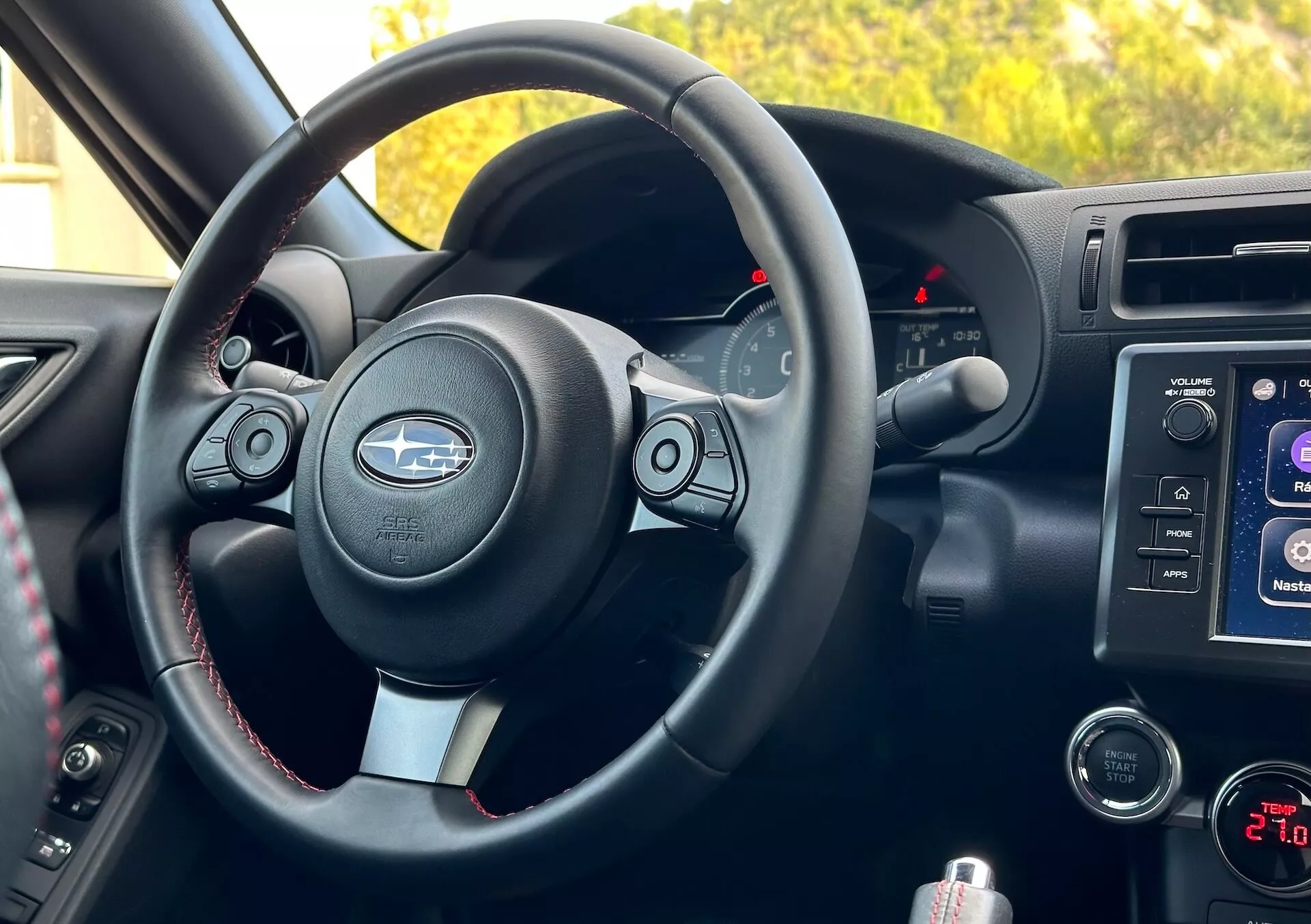 Vue intérieure de la Subaru BRZ 2023 depuis la perspective du passager montrant le volant avec des accents métalliques et le logo Subaru, boutons de commande, coutures contrastantes, tableau de bord avec indicateurs rétroéclairés, système d'infodivertissement sur la console centrale, commandes audio et climatique, et compartiment de rangement.