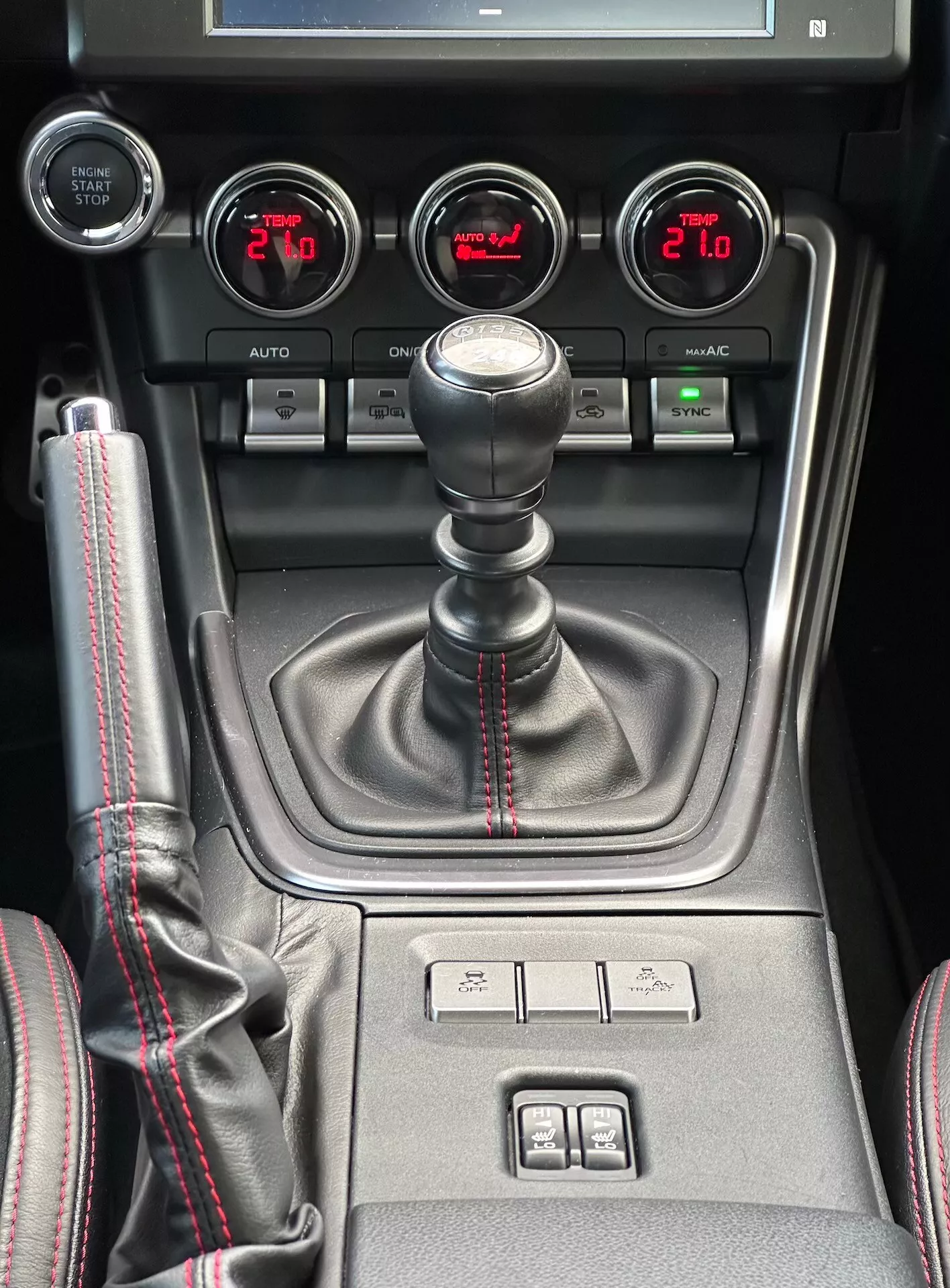 Console centrale du Subaru BRZ 2023 présentant un levier de vitesse manuel avec couture rouge sportive, jauges auxiliaires pour la pression du turbo, la tension de la batterie, la température de l'huile et le contrôle du climat à double zone en vue détaillée de l'intérieur