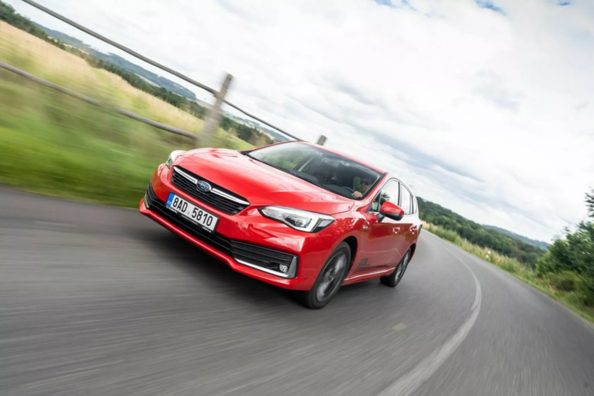 Image dynamique floue en mouvement d'une Subaru Impreza rouge de 2018 en action, vue de face montrant phare, grille et roues en alliage lors d’un virage à gauche sur une route rurale