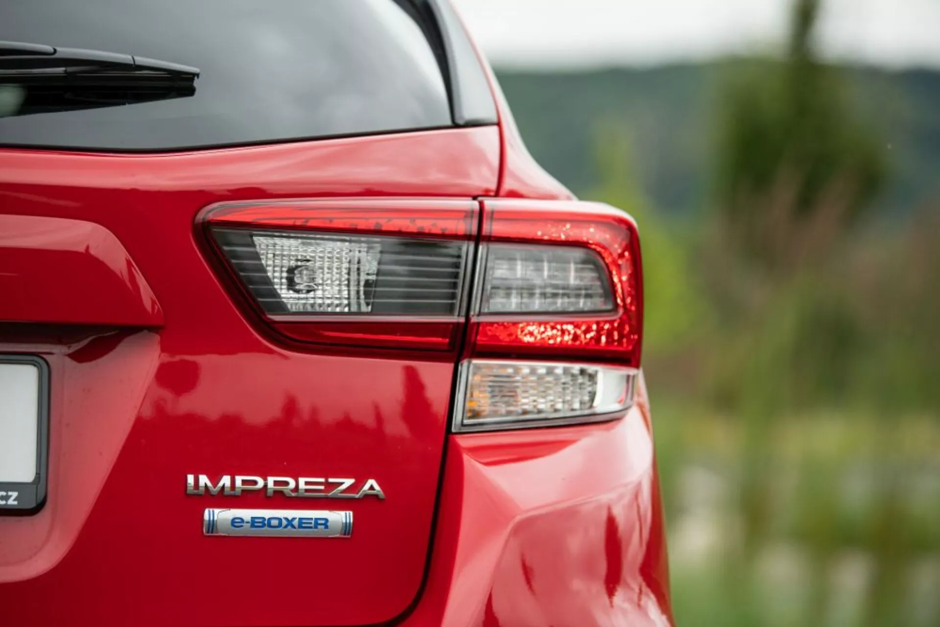 Gros plan sur le coin arrière d'une Subaru Impreza rouge de 2018, se concentrant sur le feu arrière et le badge du moteur hybride 'e-BOXER', mettant en évidence la technologie hybride avancée et l'éclairage LED de Subaru