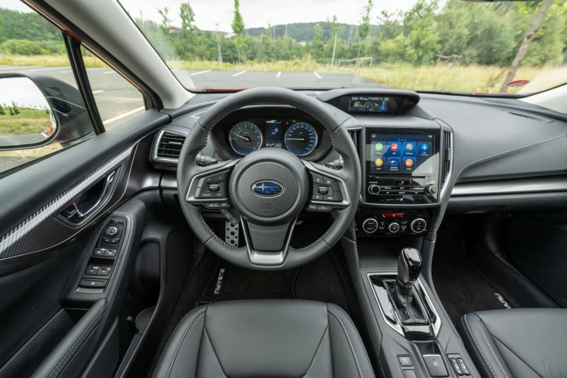 Vue intérieure de la Subaru Impreza 2018 montrant le volant avec commandes, tableau de bord numérique, système d'infodivertissement tactile, commandes de climatisation, levier de vitesse automatique et sièges en cuir avec finitions haut de gamme du point de vue du conducteur
