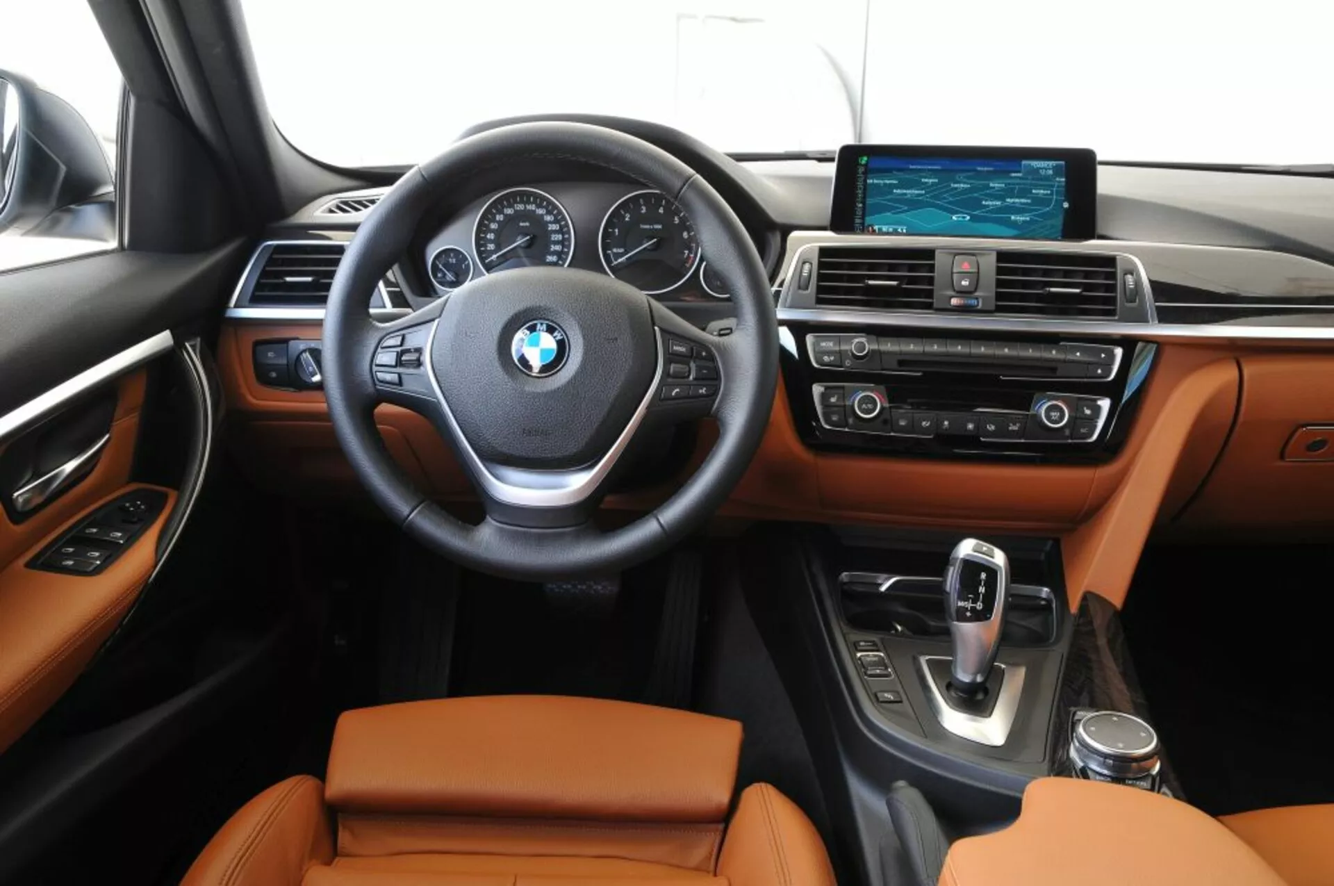 Vue frontale de l'intérieur du BMW Outback 2003 montrant la zone du conducteur et la console centrale avec des commandes montées sur le volant, des cadrans analogiques et un affichage numérique central sur le tableau de bord, un système d'infodivertissement à écran large et des sièges en cuir
