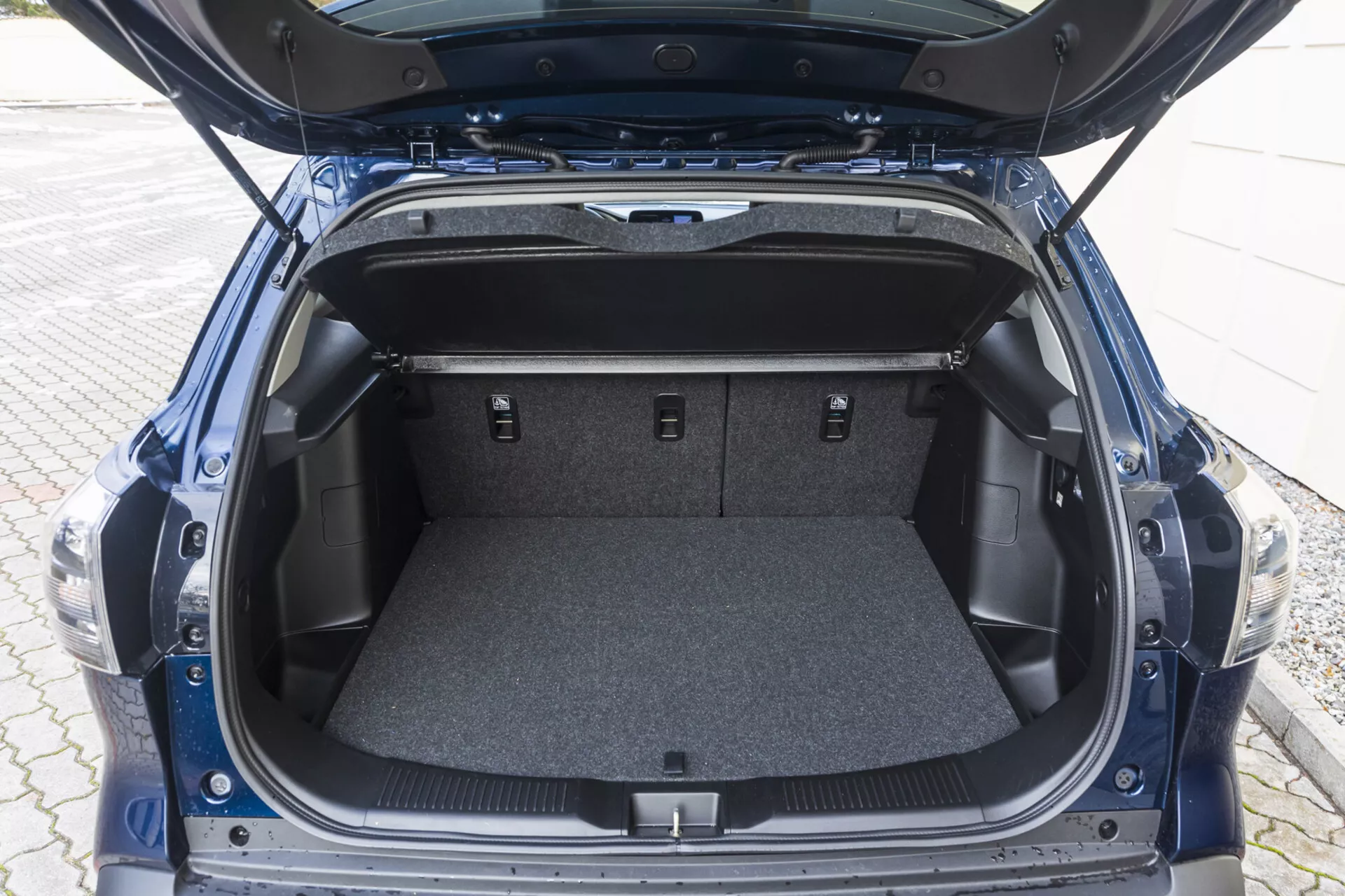 Vue de l'espace de coffre arrière de Suzuki S-Cross 2022 avec le couvercle ouvert montrant une zone tapissée vide, des compartiments latéraux et des sièges arrière rabattus