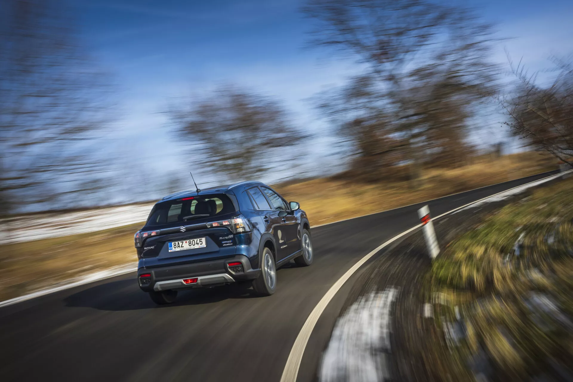 SUV moderne Suzuki S-Cross 2022 en mouvement, montrant le profil vue arrière trois-quarts avec roues tournantes lors d'une journée claire