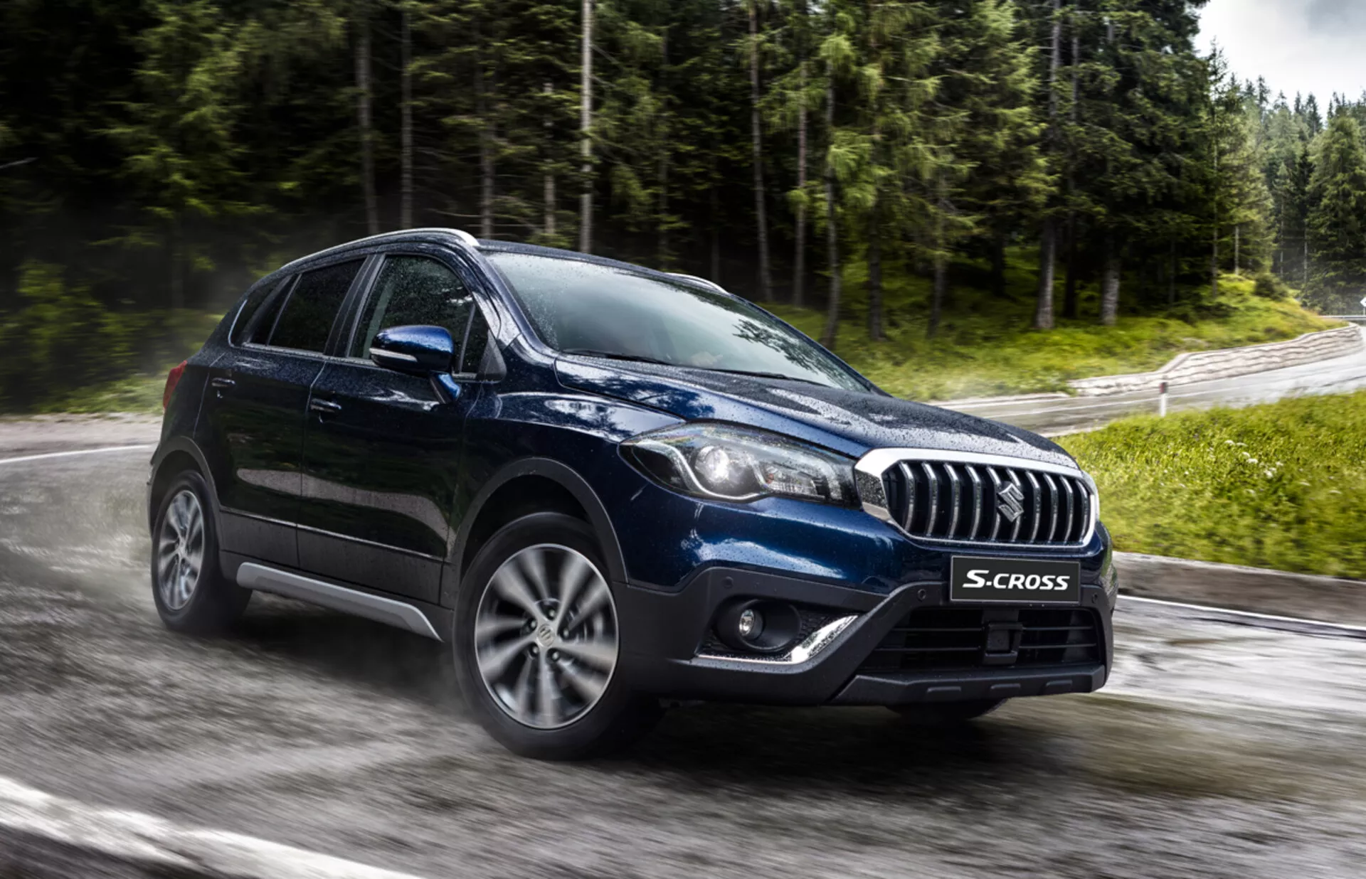 Suzuki S-Cross 2022 capturé d'un angle avant trois-quarts, mettant en évidence sa grille accentuée de chrome, ses phares modernes LED ou HID, ses roues en alliage à multiples rayons et sa forme robuste de crossover sur une route mouillée et entourée de verdure, suggérant une technologie avancée et une capacité tout-temps.