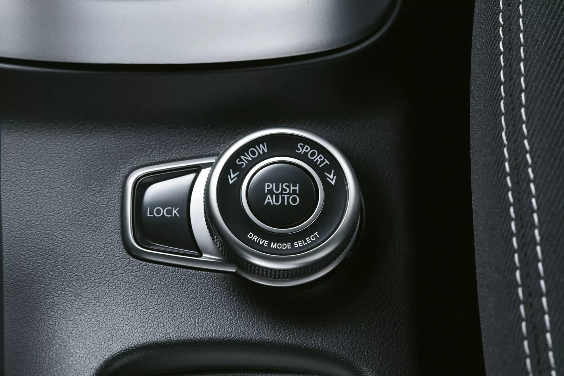 Vue rapprochée de l'intérieur du Suzuki S-Cross 2022 montrant le sélecteur de mode de conduite étiqueté 'PUSH AUTO' avec les options 'SNOW' et 'SPORT', à côté d'un bouton 'LOCK', sur un panneau de qualité en tons sombres, possiblement texturé comme du cuir avec des coutures visibles.