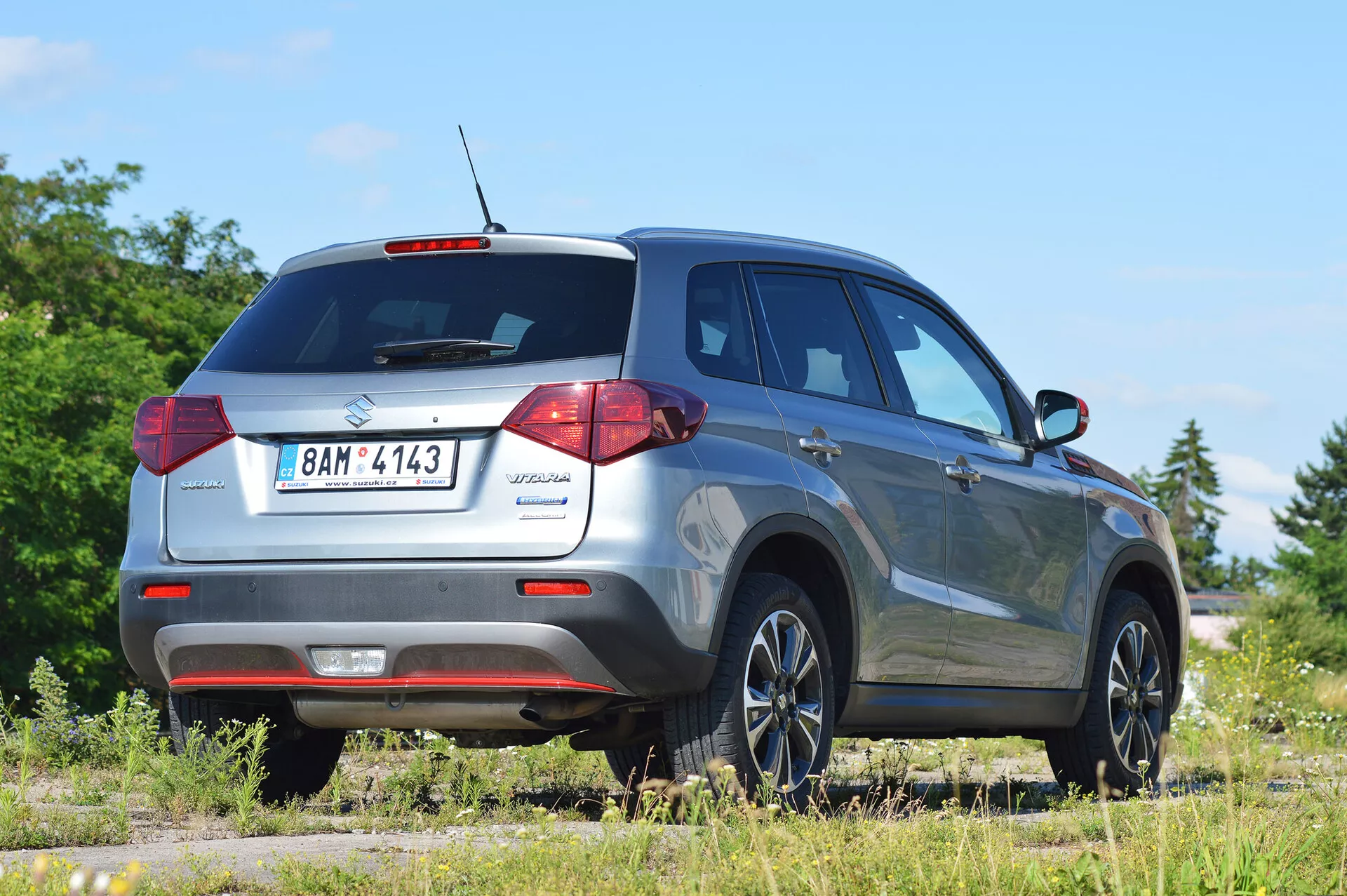 Suzuki Vitara 2018 capturée sous un angle trois quarts arrière droit, mettant en évidence le design des feux arrière, la lunette arrière et le profil du côté passager. L'image montre les commodités modernes du SUV compact telles qu'une antenne de toit pour les fonctionnalités technologiques, des capteurs de stationnement arrière et des roues en alliage élégantes. Le véhicule est positionné sur une surface non pavée dans un environnement rural, indiquant son potentiel tout-terrain. Idéal pour les catégories automobiles, SUV et les images de véhicules tout-terrain.