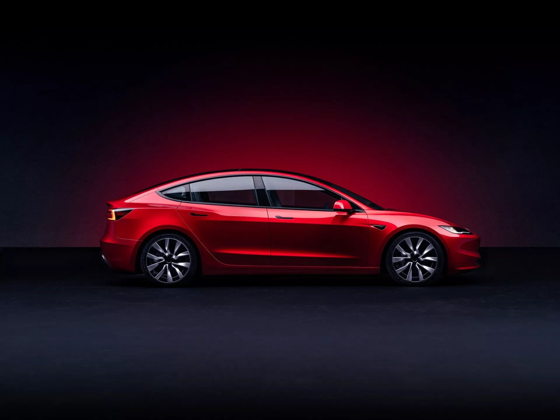 Facelift de première génération de la Tesla Model 3 2023, berline rouge avec toit panoramique et éclairage LED, vue de profil latéral en studio sur fond dégradé sombre, équipée de roues en alliage et de technologie avancée pour véhicule électrique