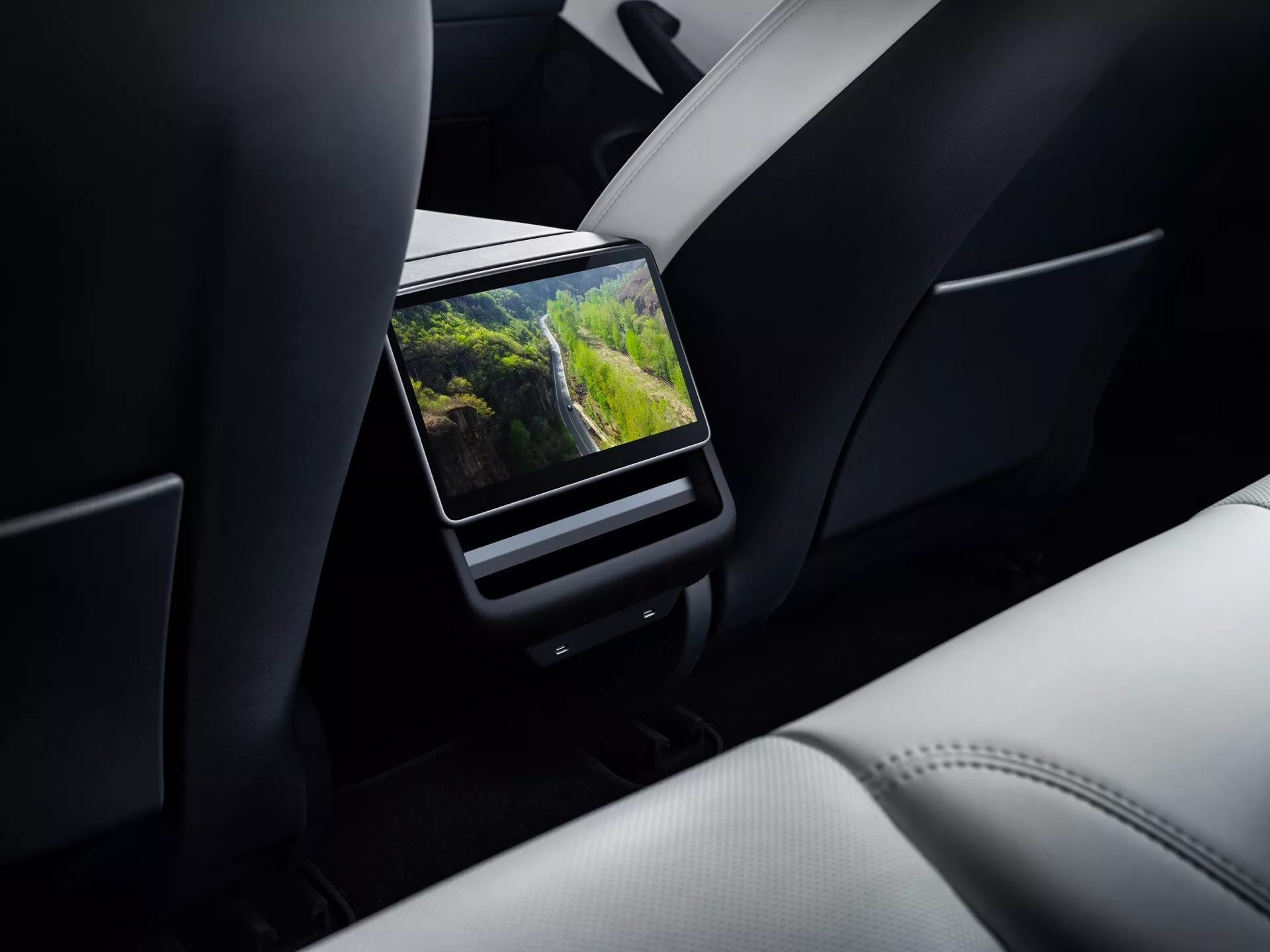 Tesla Model 3 (1ère génération restylée) 2023 présentant de près un système de divertissement arrière OEM dans la voiture avec écran haute résolution entre le siège passager avant et le conducteur, affichant une scène extérieure vibrante dans une cabine luxueuse avec garniture en cuir haut de gamme.