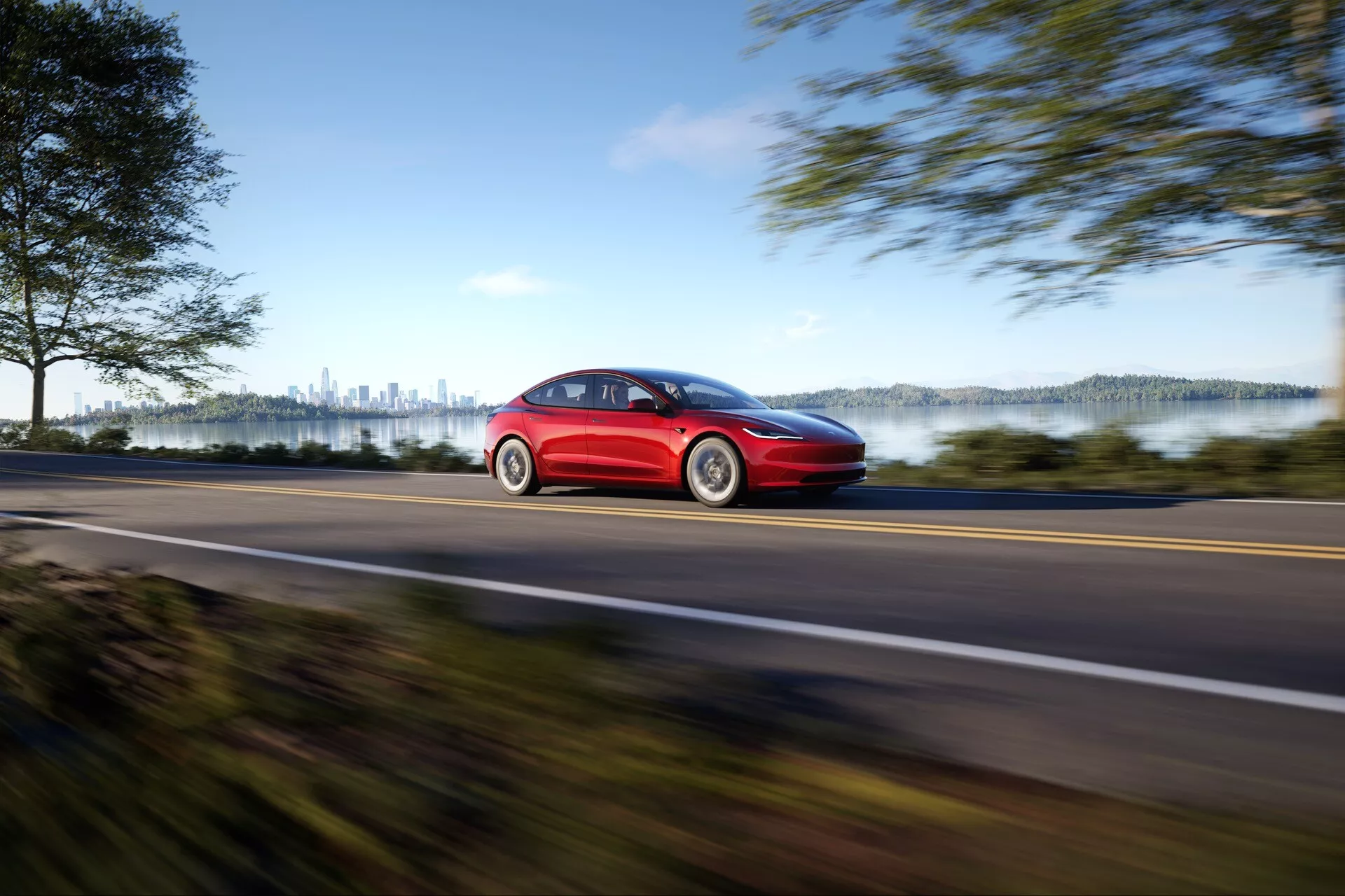 Tesla Model 3 2023 (1ère génération, restylée) en rouge, illustrant la vitesse avec effet de flou sur route rurale, vue de profil