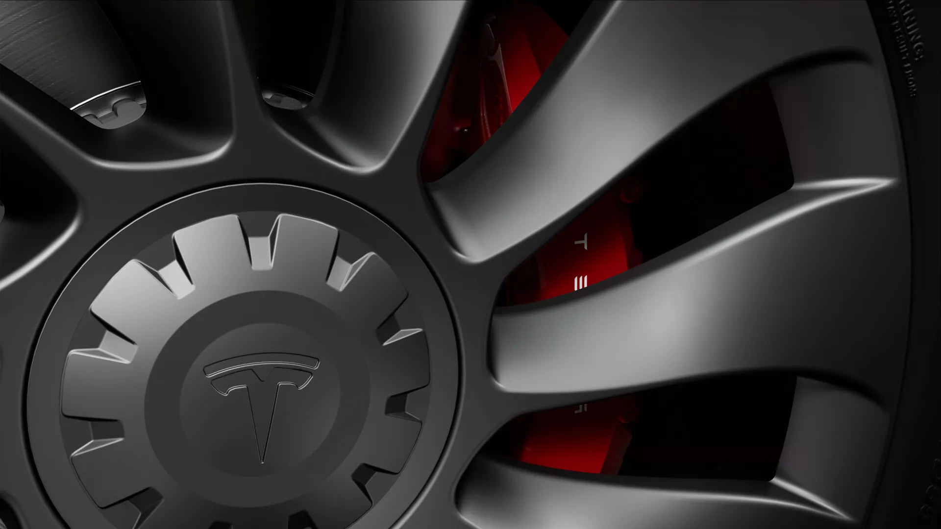 Vue en gros plan de la roue d'une Tesla Model-3 2019 (1ère génération), montrant une jante multi-rayons haute performance avec une finition mate foncée, indicative d'une esthétique sportive ou haut de gamme. Le design complexe en forme de turbine aide au refroidissement des freins et à l'aérodynamisme. Le capuchon central est intentionnellement obscurci pour masquer la marque. Derrière les rayons, on aperçoit partiellement un étrier de frein rouge, signe d'un système de freinage orienté performance. On aperçoit un disque de frein ventilé, conçu pour dissiper la chaleur de manière efficace, et le bord du pneu à profil bas est à peine visible. L'éclairage dramatique met en valeur la texture et la forme, soulignant la prouesse technologique des composants de la roue et du frein.