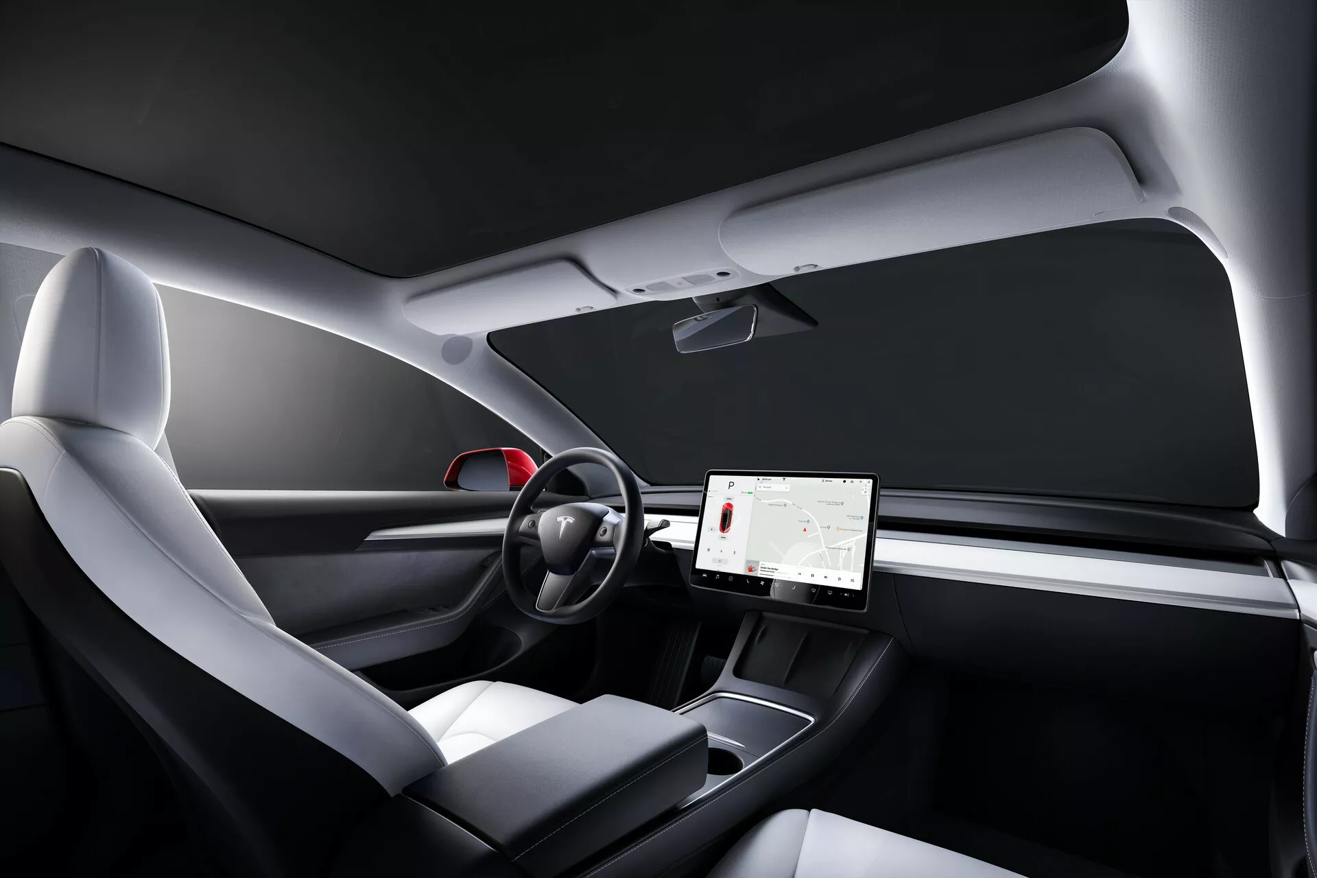 Vue intérieure de la Tesla Model 3 2019 (1ère génération) depuis la perspective du passager, mettant en avant un design de tableau de bord minimaliste, un grand écran tactile central, un volant à deux branches avec commandes tactiles, des sièges ergonomiques modernes avec revêtement en matériaux mixtes, une console centrale épurée, des touches de décor en bois et un toit en verre panoramique.