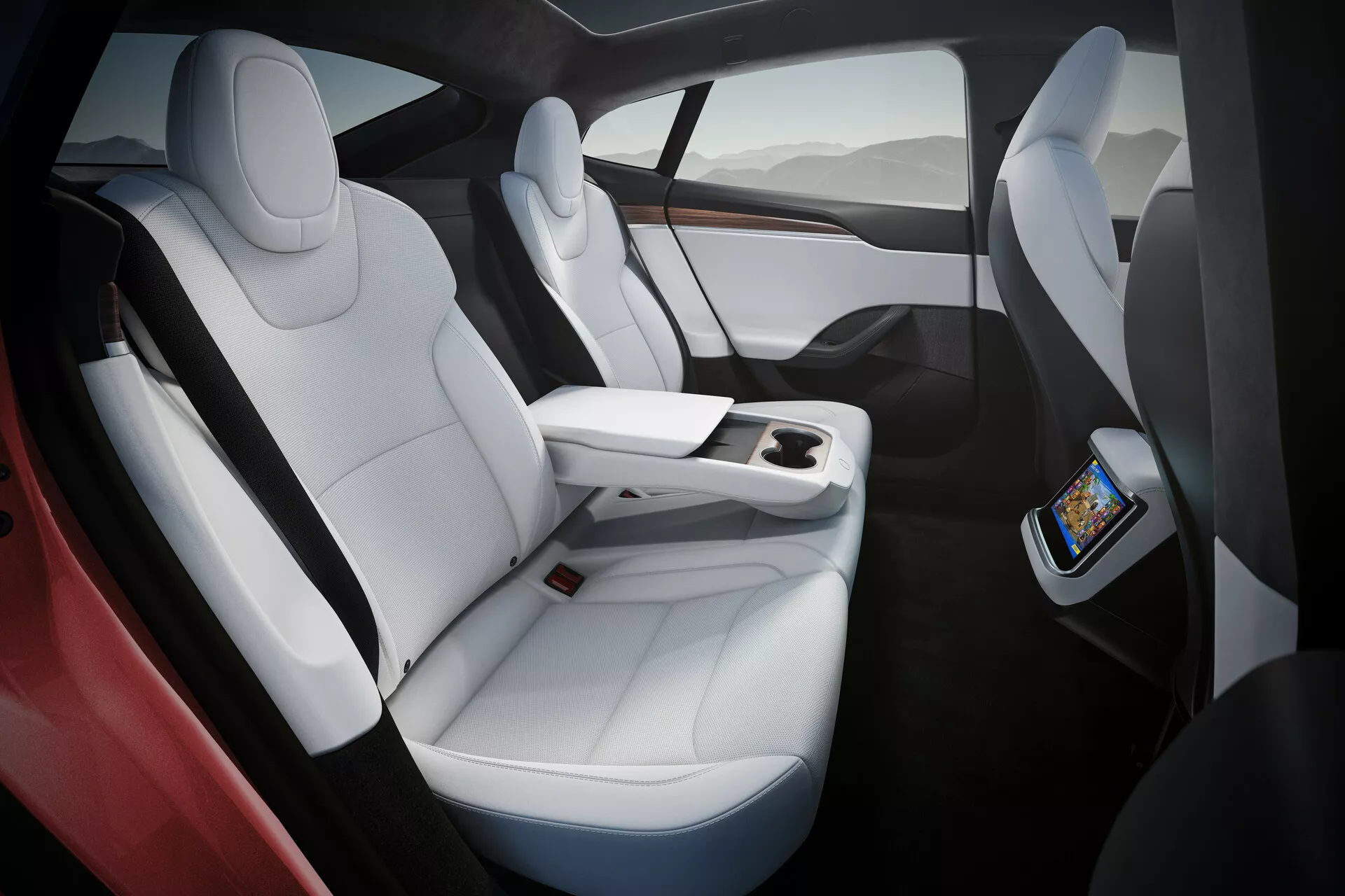 Intérieur de la Tesla Model S 2016 (1ère génération facelift) présentant des sièges en cuir blanc de luxe avec des accents noirs, un design ergonomique et un espace généreux pour les jambes. L'image capture les sièges du côté droit sous un angle légèrement surélevé, mettant en avant la console centrale fonctionnelle se terminant avant les sièges arrière, avec un écran tactile pour les passagers arrière et une recharge sans fil pour smartphones. Toit panoramique en verre offrant une lumière naturelle et une sensation de légèreté.
