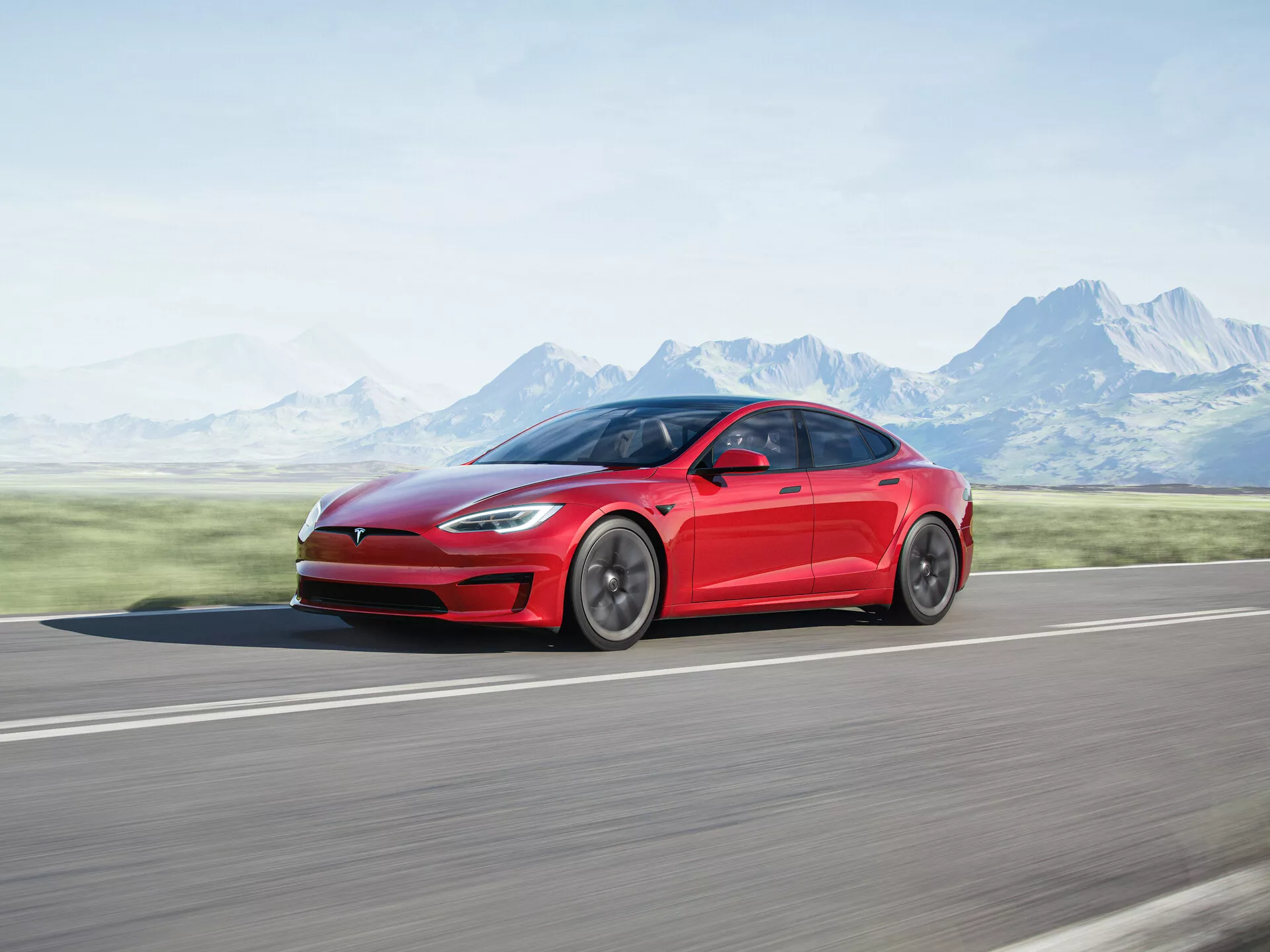 Image de profil latéral d'une berline électrique Tesla Model S 2016 (1ère génération facelift) rouge, capturée en mouvement. Le design élégant et aérodynamique de la voiture est mis en valeur, avec des lignes fluides du garde-boue avant à l'arrière et des jantes polies. Photographié sur une route en asphalte avec un arrière-plan flou de montagnes et un ciel clair, soulignant la vitesse et le mouvement du véhicule.