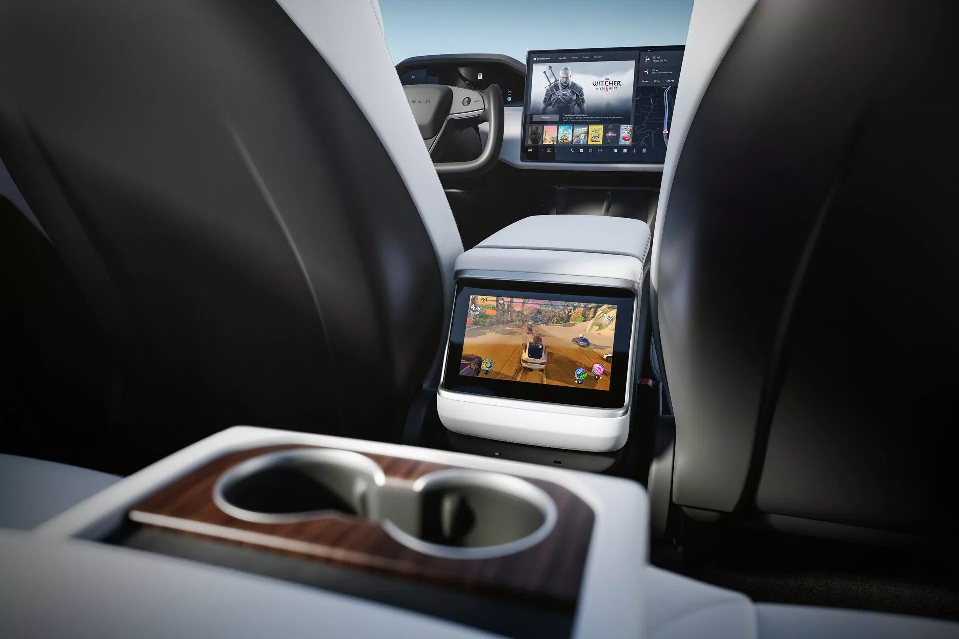 Vue intérieure de la Tesla Model S 2016 (première génération facelift) axée sur le compartiment des passagers arrière. Perspective à partir du siège arrière à hauteur de coussin montrant deux sièges avant avec appuis-tête, console centrale et écran intégré à l'arrière du siège passager avant. Technologie de divertissement pour les sièges arrière visible avec écran actif montrant du contenu multimédia. Caractéristiques incluant accoudoir pliable avec porte-gobelets intégrés et finition en bois, vue partielle du tableau de bord avant avec écran d'infodivertissement plus grand et matériaux de luxe. Intérieur bien éclairé avec des tons neutres indiquant un véhicule de luxe contemporain.