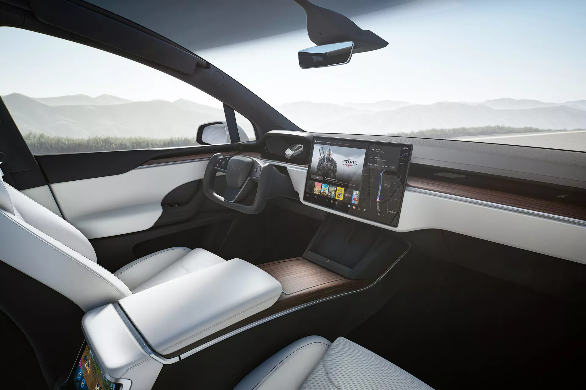 L'intérieur d'une Tesla Model X 2021, vu depuis un angle légèrement incliné vers le côté passager, montre un tableau de bord moderne avec un grand système d'infodivertissement à écran tactile monté au centre affichant des graphiques colorés. Le siège passager avant, enrobé de blanc, contraste élégamment avec le tableau de bord plus sombre et la finition en bois. Un smartphone repose sur un probable chargeur sans fil sur la console centrale dégagée, et les grandes fenêtres avant contribuent à une sensation de cabine aérée et ouverte. Le rétroviseur central fin situé en haut du pare-brise suggère des fonctionnalités avancées telles que la réduction automatique de l'éblouissement ou un affichage caméra arrière.