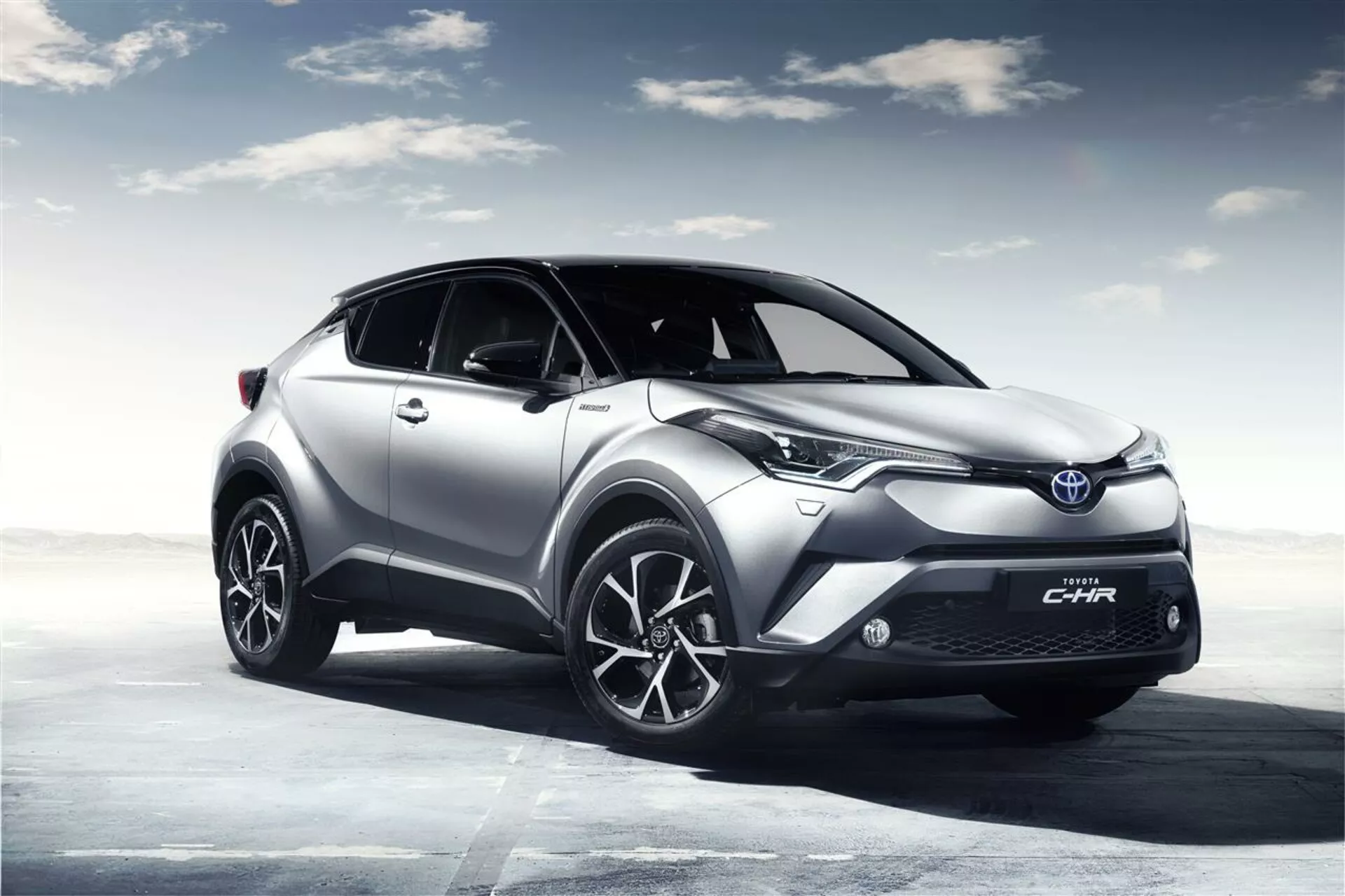 Toyota C-HR 2016 argenté en pose trois-quarts avant montrant les phares LED, les roues en alliage, et le design élégant sur fond de ciel généré par ordinateur, soulignant ses caractéristiques sportives et modernes.