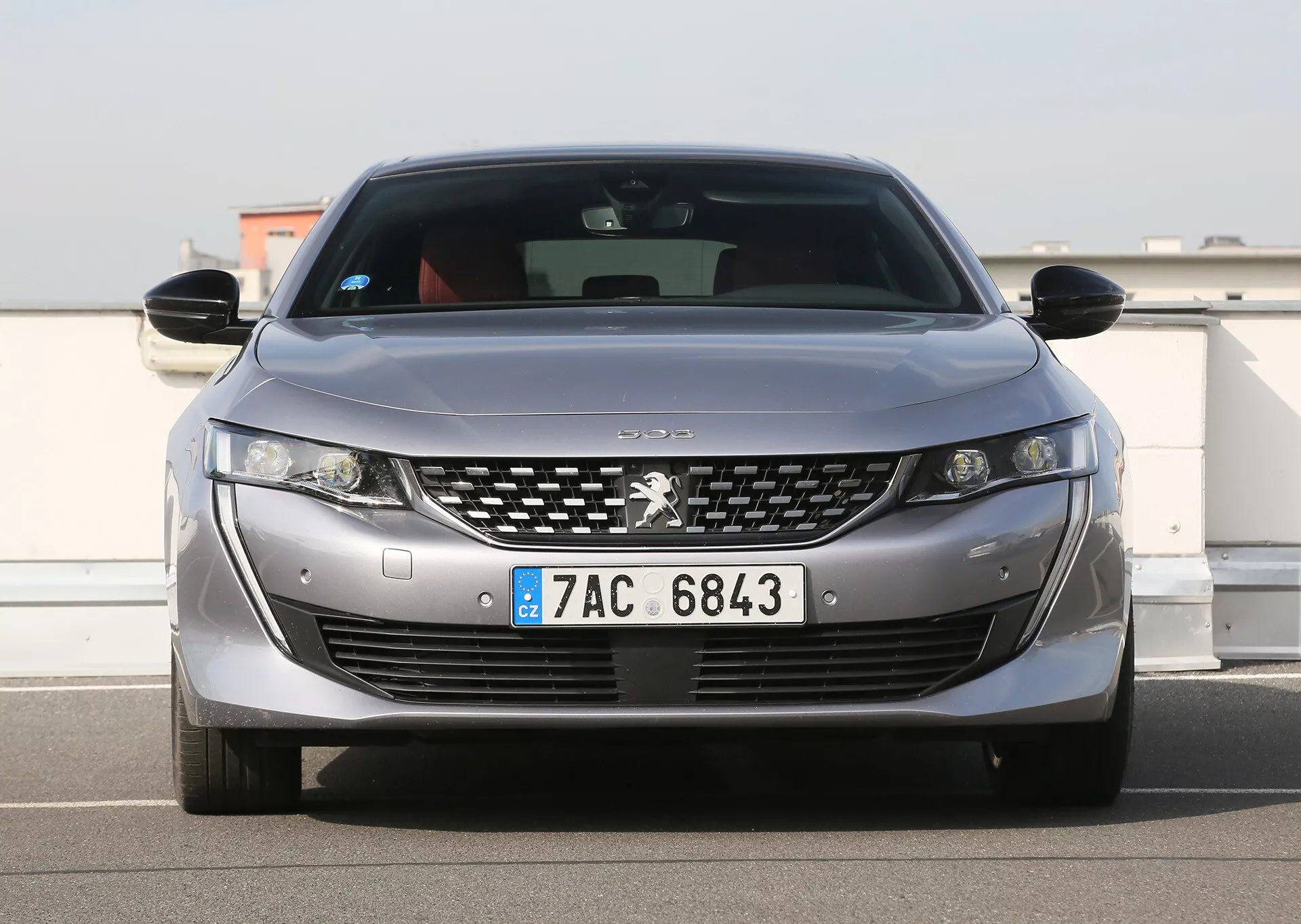 Vue de face d'une Peugeot argentée avec phares LED, grille détaillée chromée, capteurs de stationnement et plaque d'immatriculation européenne, mettant en avant des caractéristiques de design et technologie modernes, stationnée en extérieur sous un ciel clair